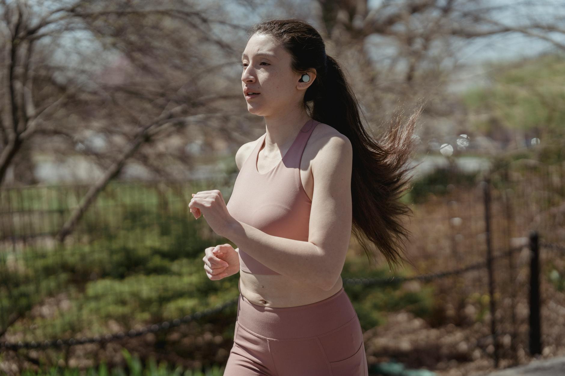 A woman jogs outdoors with wireless earbuds, embodying a healthy lifestyle. - spring running for beginners