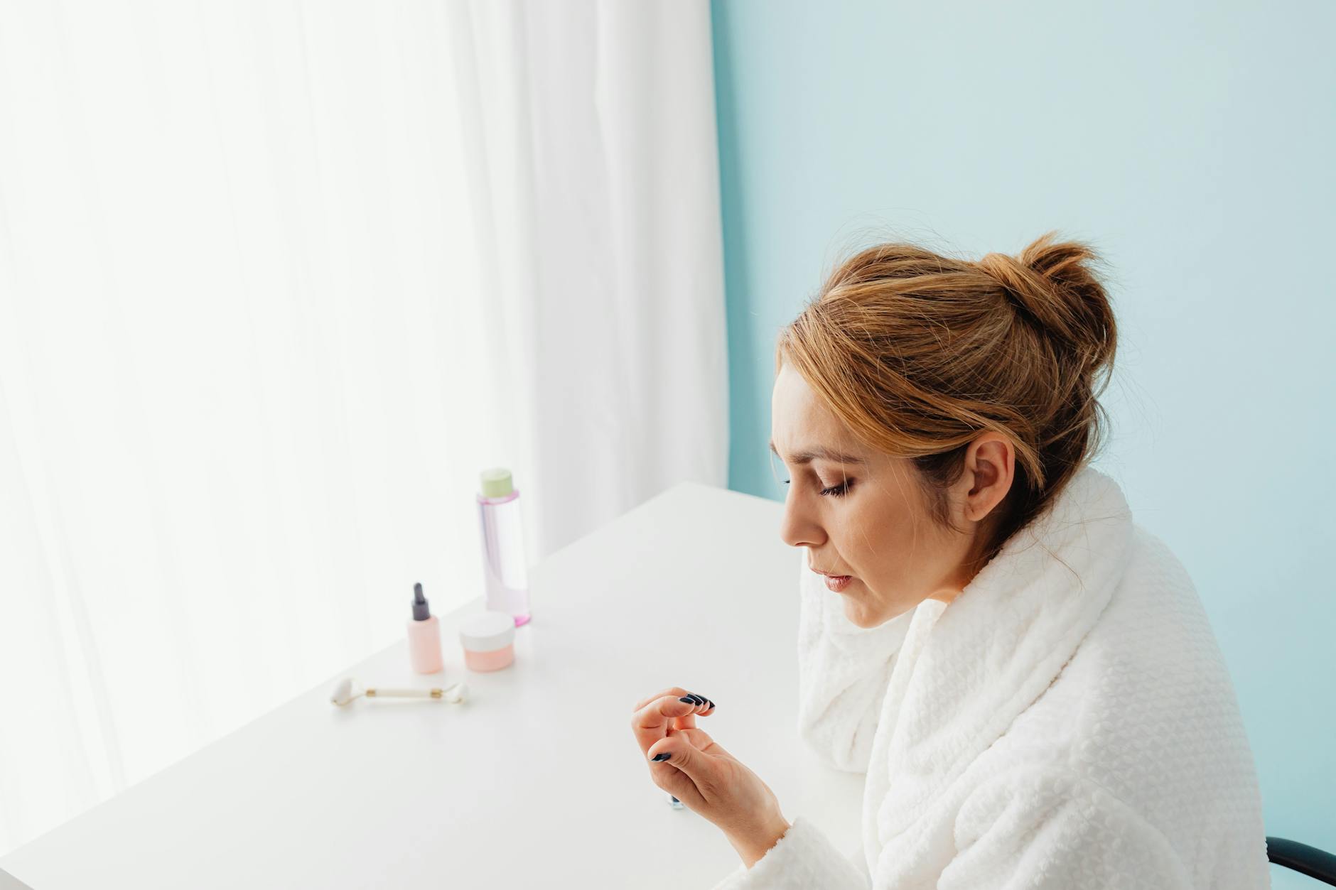 Woman wearing a bathrobe applying skincare products indoors, focusing on her daily beauty routine. - spring skincare routine