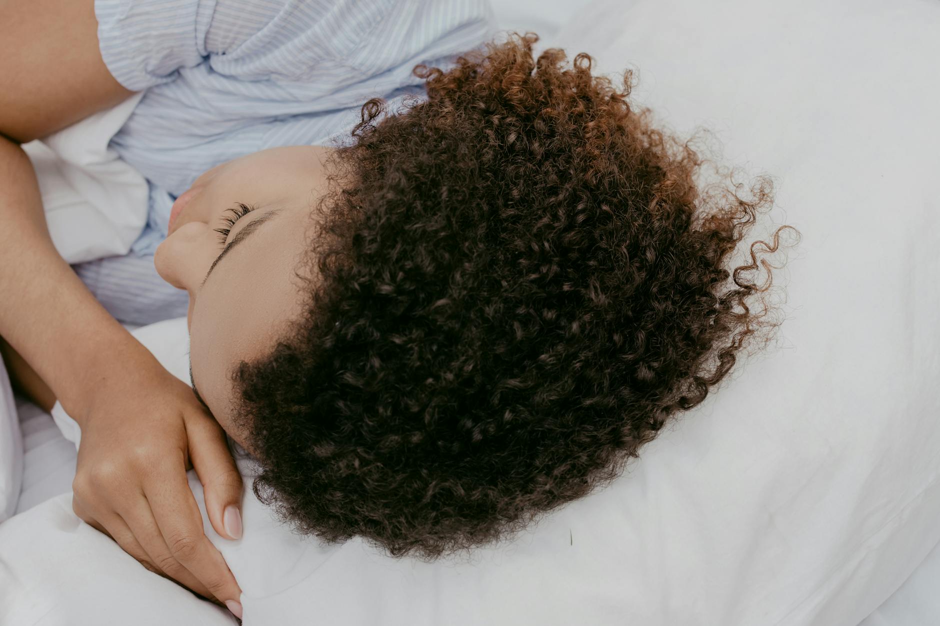 A woman resting peacefully on a pillow, showcasing natural curly hair from a close-up angle. - spring sleep schedule