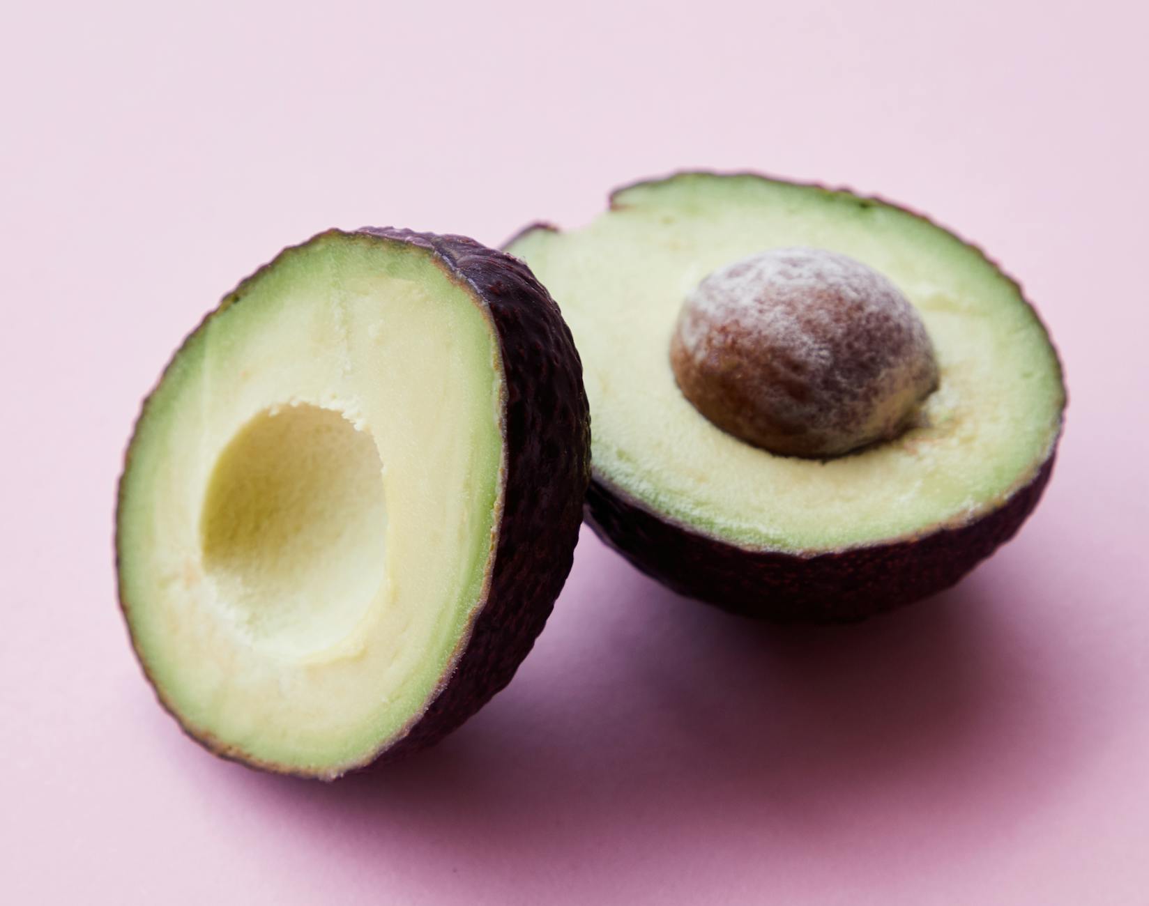 High angle of healthy ripe avocado with seed casting shadow on pink background - spring superfoods skin