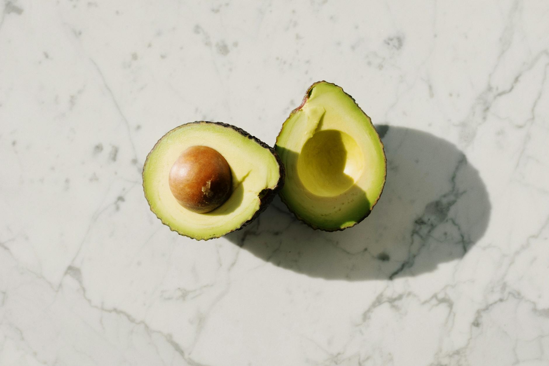 Sliced avocado with seed on a marble background, showcasing healthy eating. - spring superfoods skin