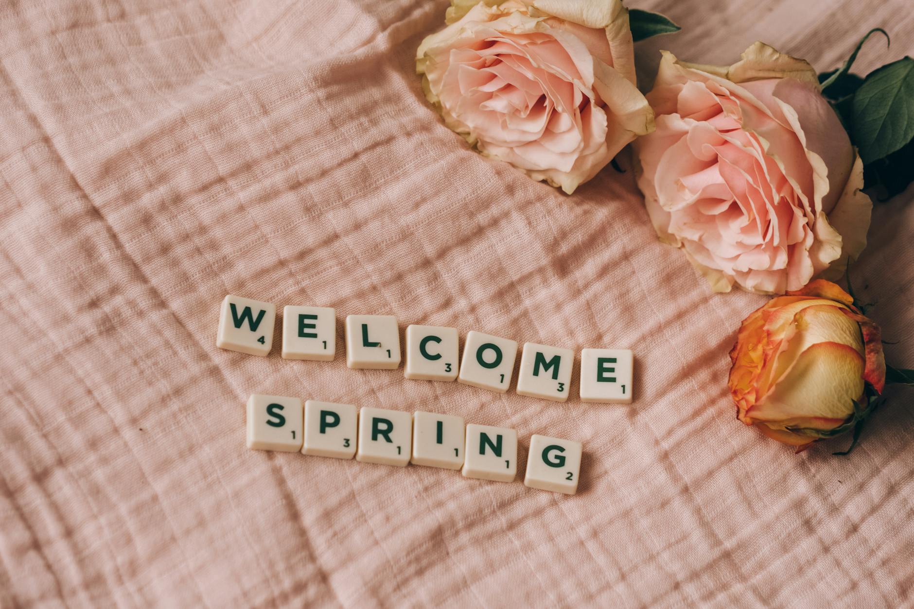 Pink roses and scrabble tiles spelling 'Welcome Spring' on a soft pink fabric background. - spring wellness reset