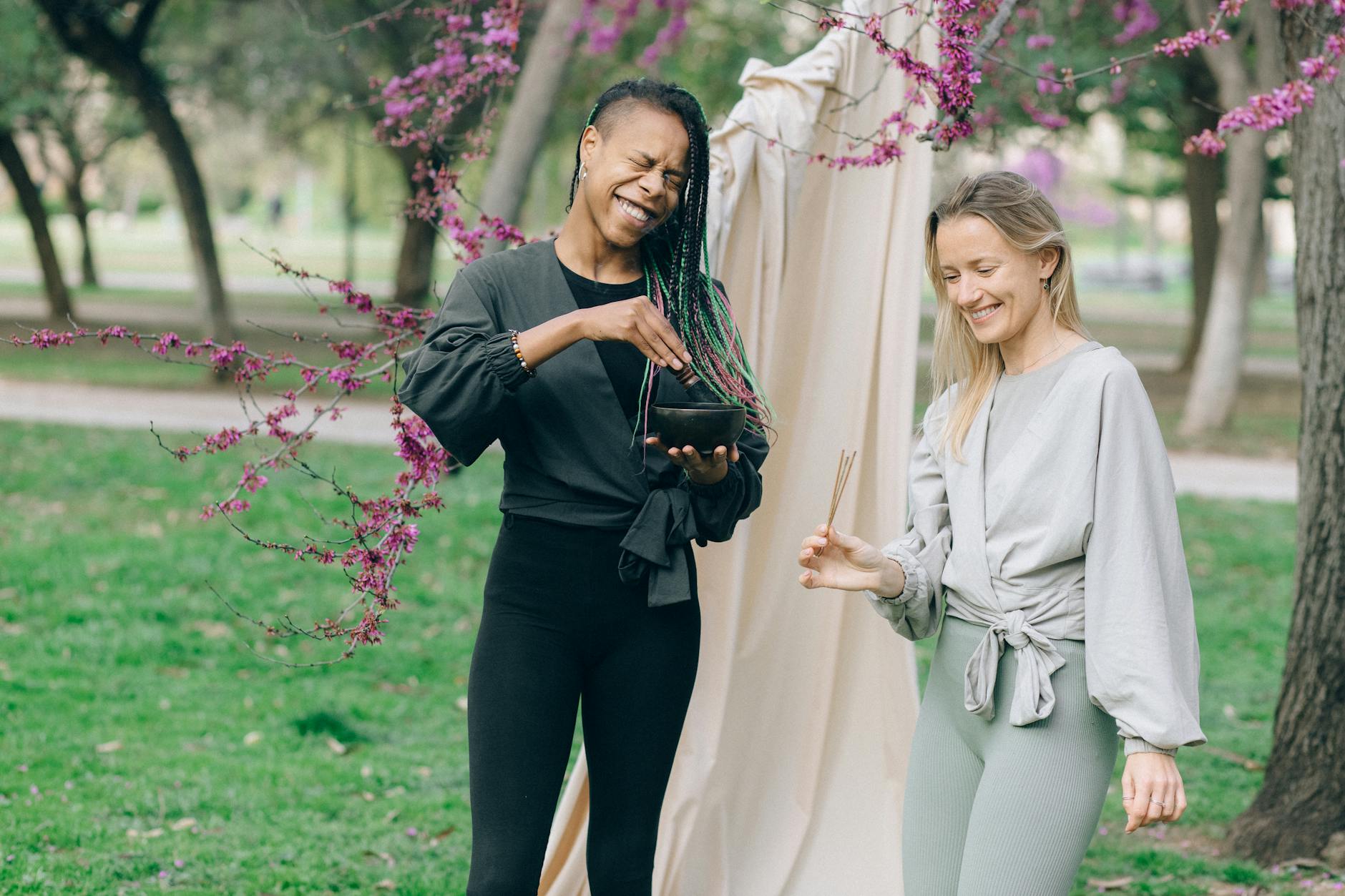Two women enjoying aromatherapy amidst blooming trees in a serene outdoor park setting. - spring wellness reset