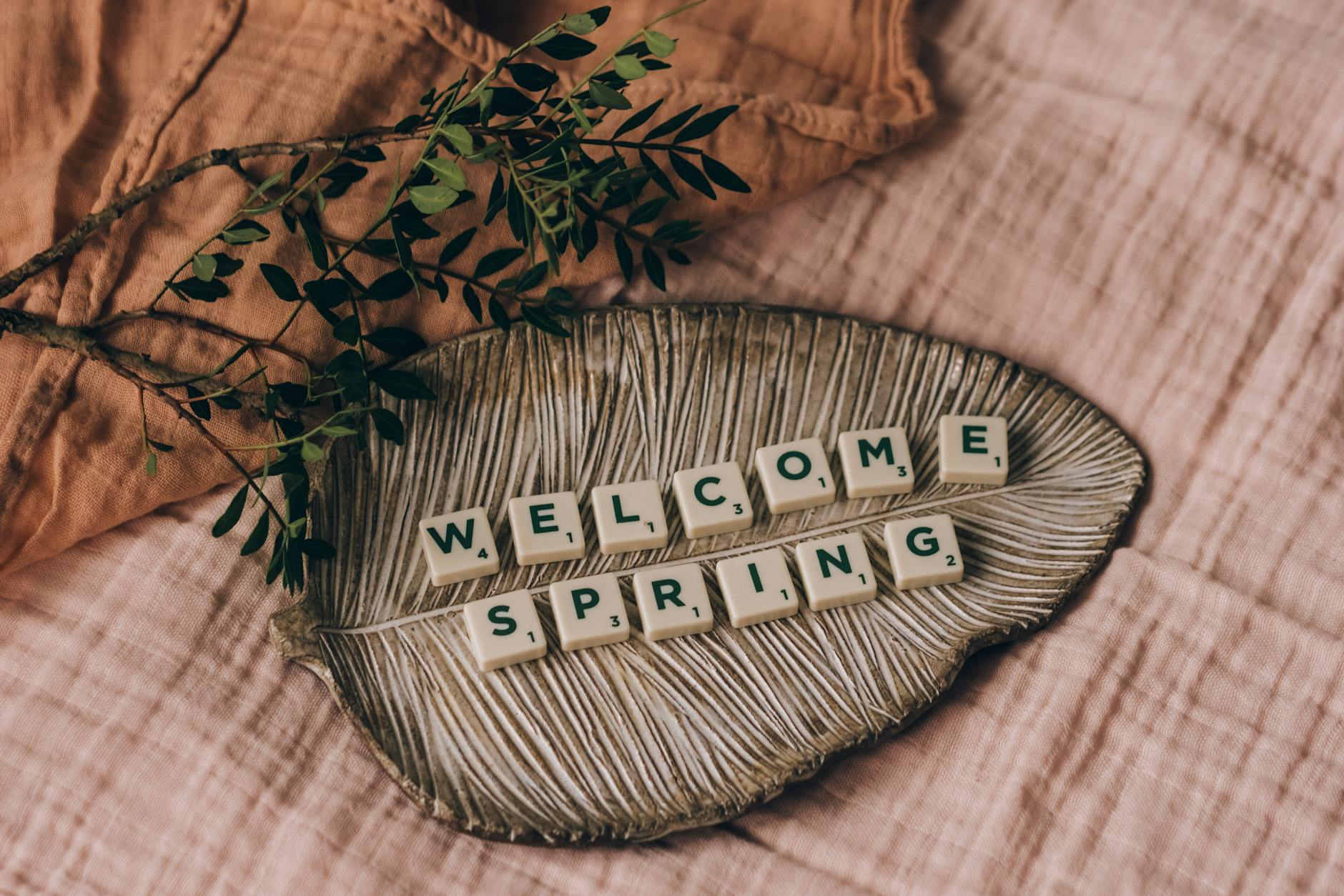 Tiles spelling 'Welcome Spring' on a leaf-shaped tray with greenery. - spring wellness reset
