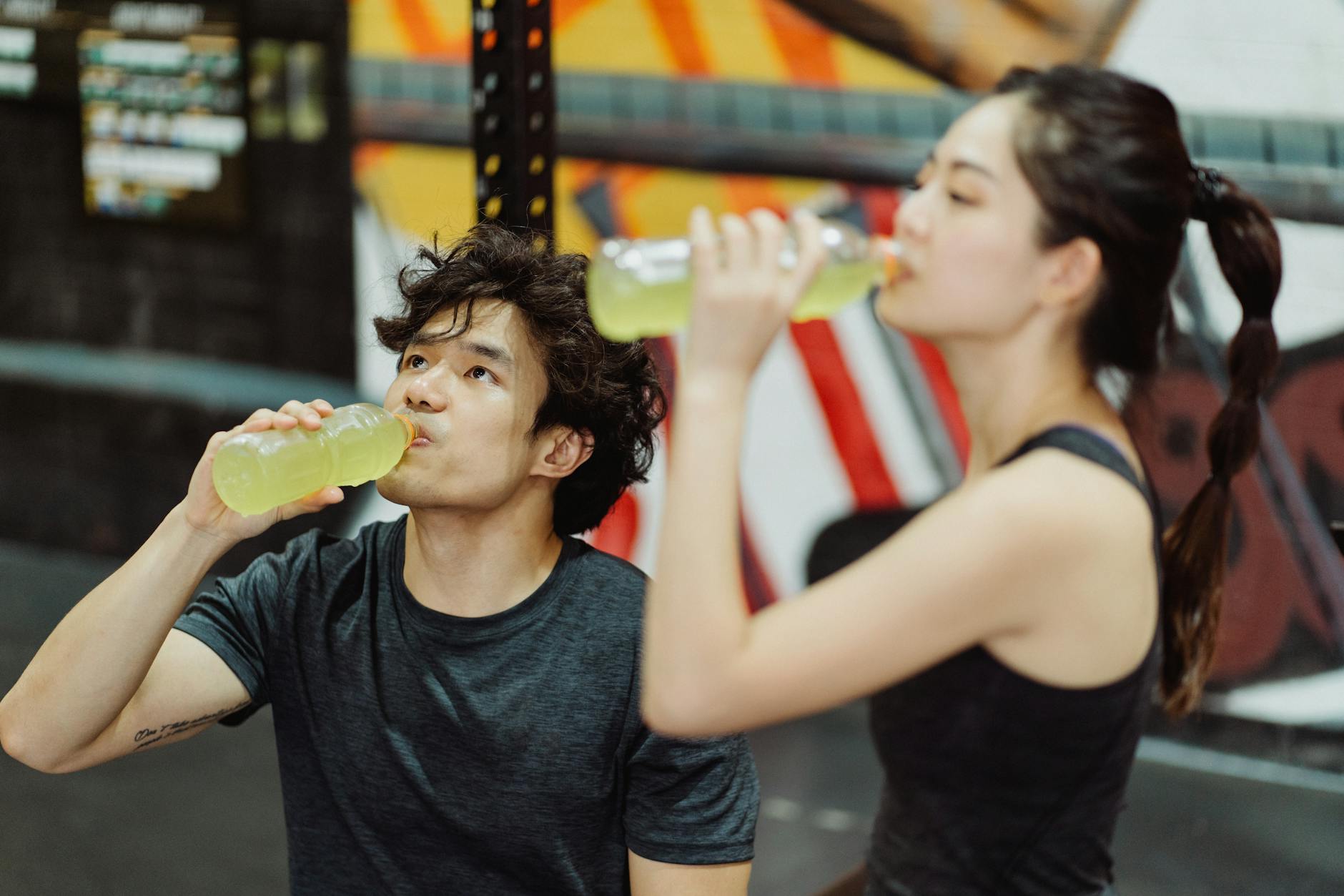 Fit Asian couple hydrating at the gym after an intense workout. Refreshing drink break. - spring workout hydration