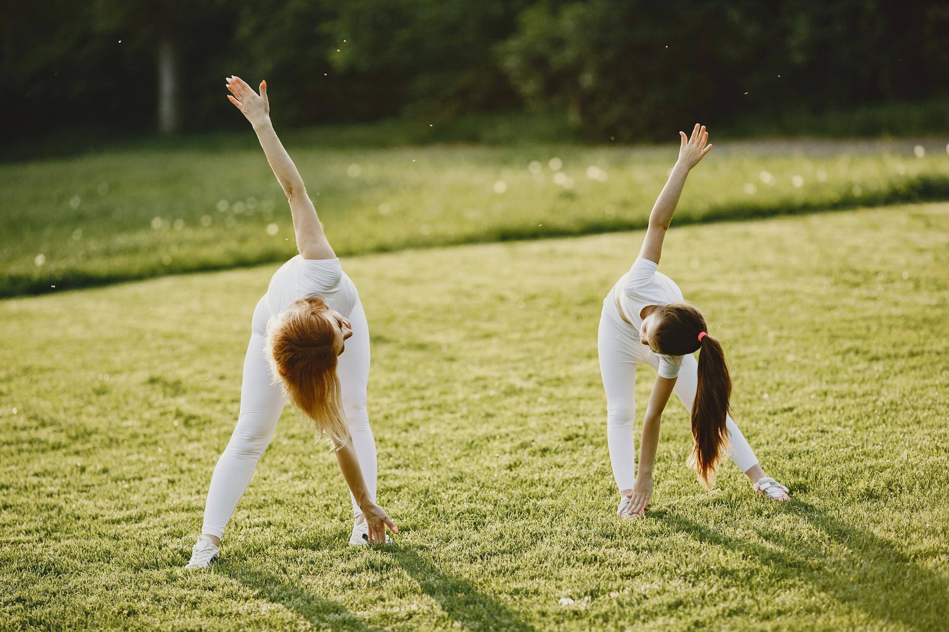 A mother and daughter bond while stretching in a sunny grass field, dressed in white activewear. - spring workouts busy mornings