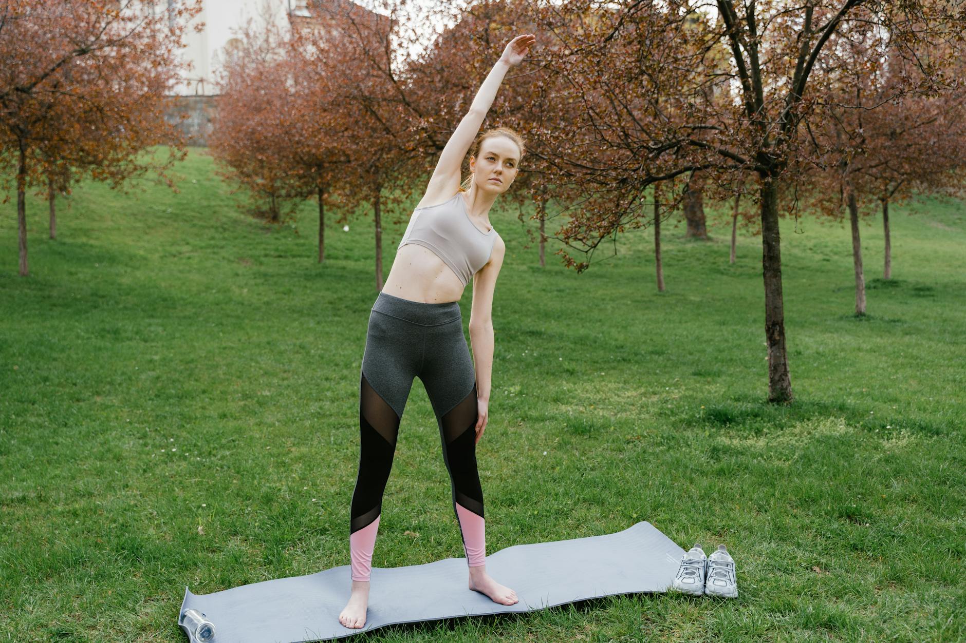 Woman in activewear performing side stretch on yoga mat in a park setting - spring workouts busy mornings