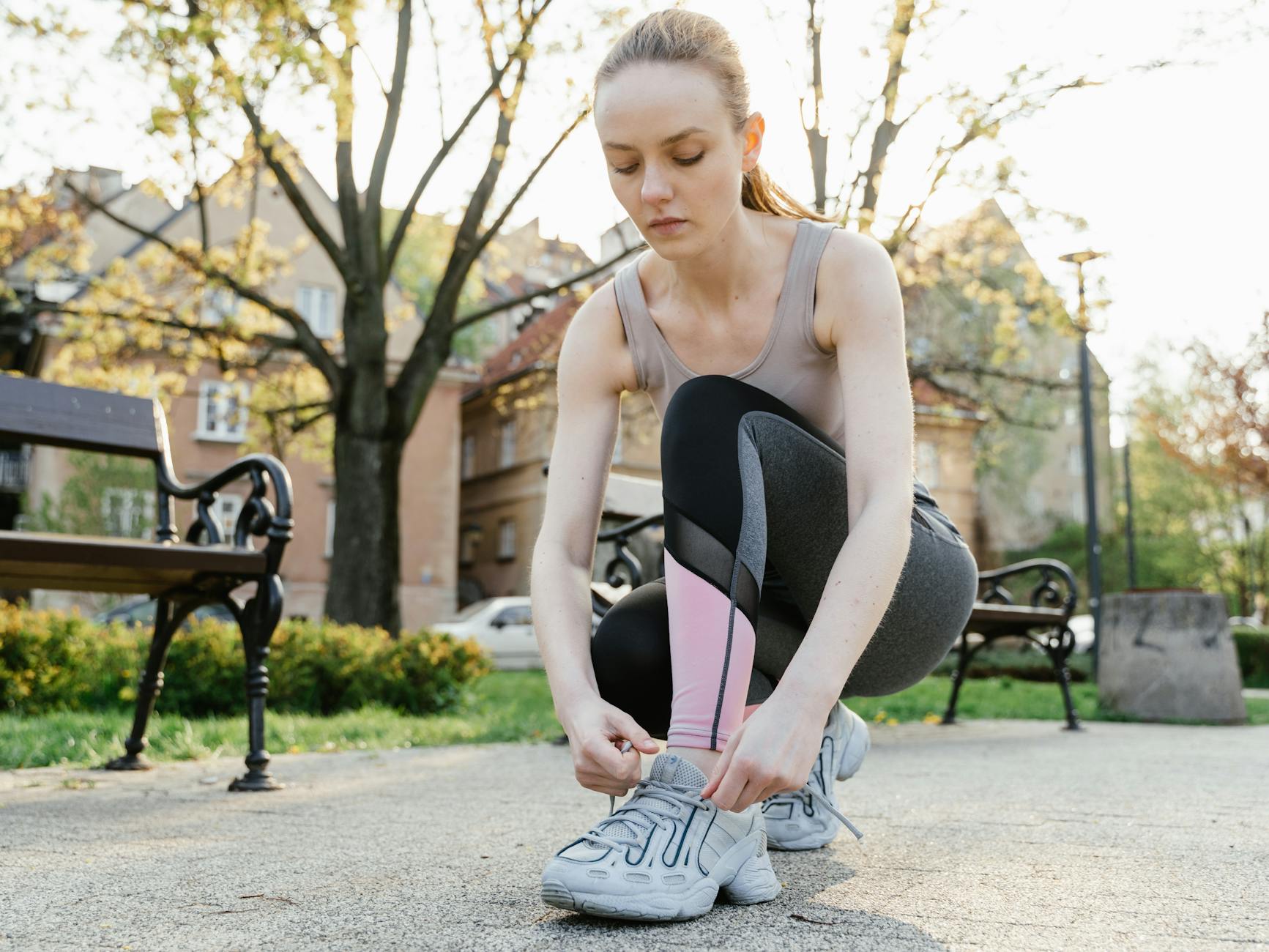 Woman in activewear tying sneakers outdoors in a park, preparing for a run. - spring workouts busy mornings