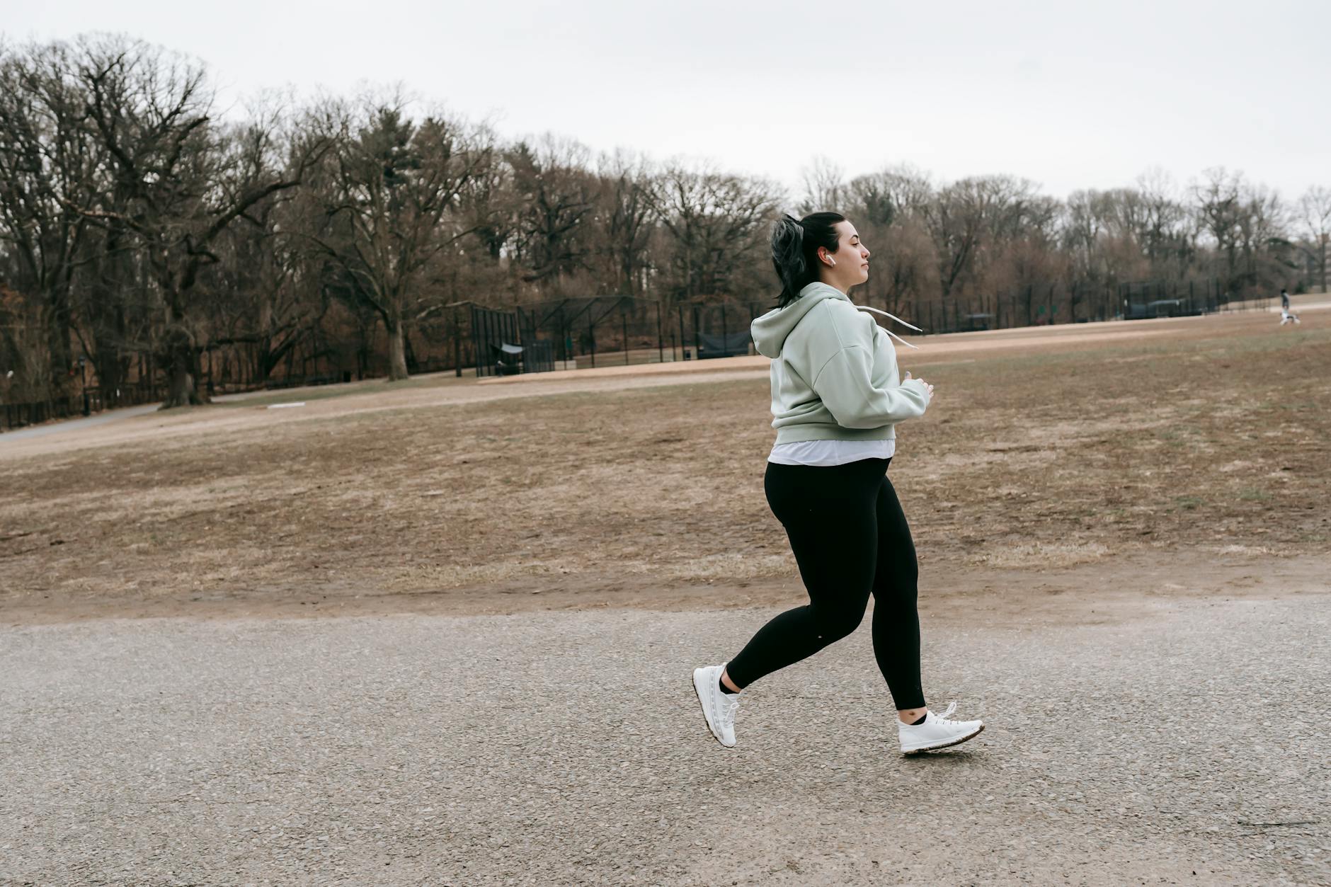 Side view of overweight young female jogging in park with leafless trees in autumn - spring workouts busy mornings