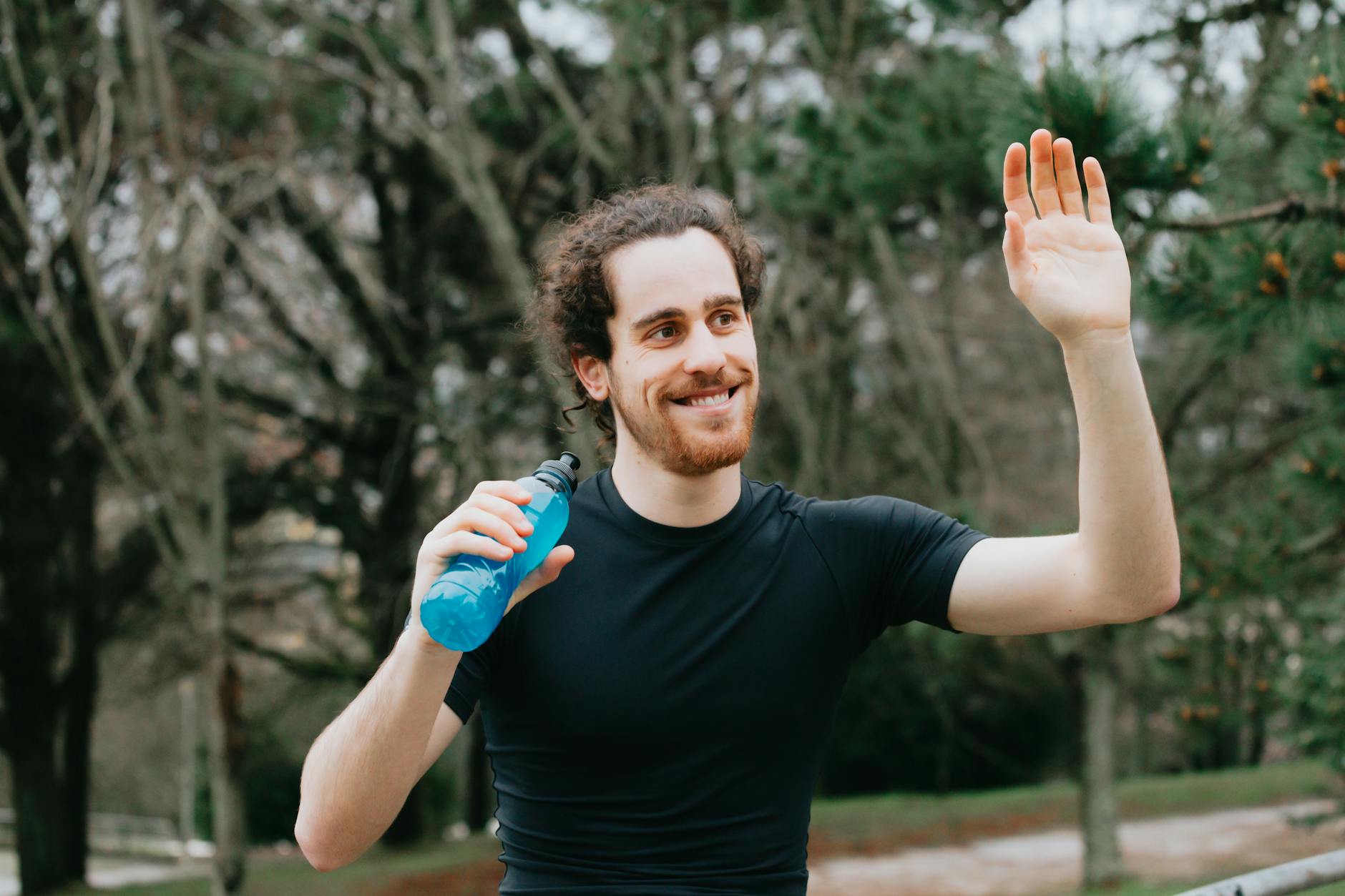 Man in a park waving while holding a water bottle, expressing joy and friendliness. - staying hydrated spring