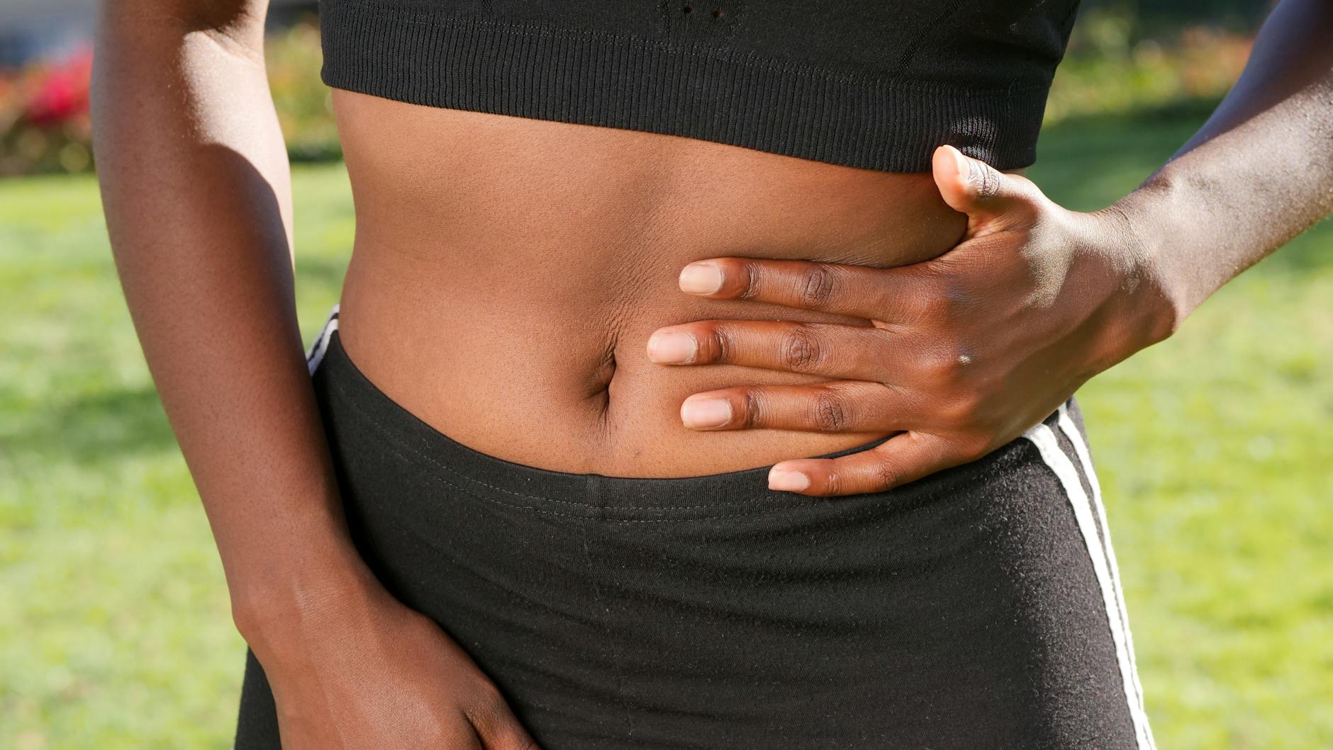 Close-up of a person holding their abdomen, indicating stomach discomfort, outdoors. - stomach fat workout