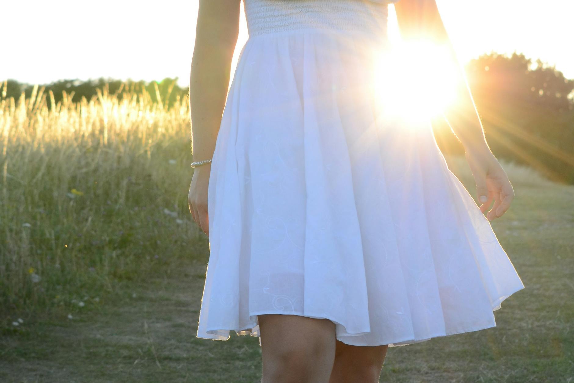 A woman in a white dress stands in a field, illuminated by the soft glow of the sunset. - sunlight weight loss