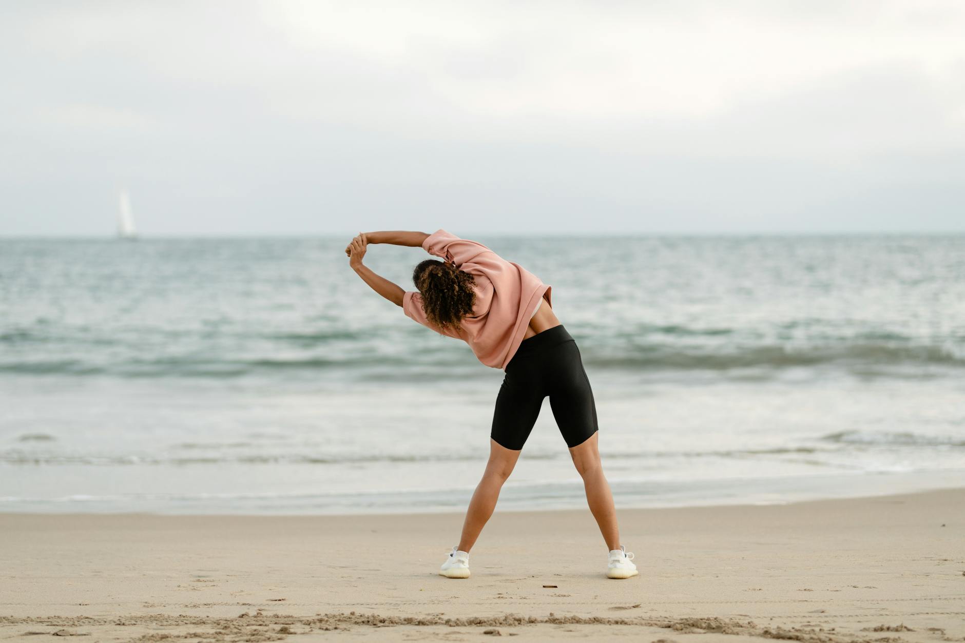 A woman stretching on the beach with a scenic ocean view at sunrise. - sunrise workouts