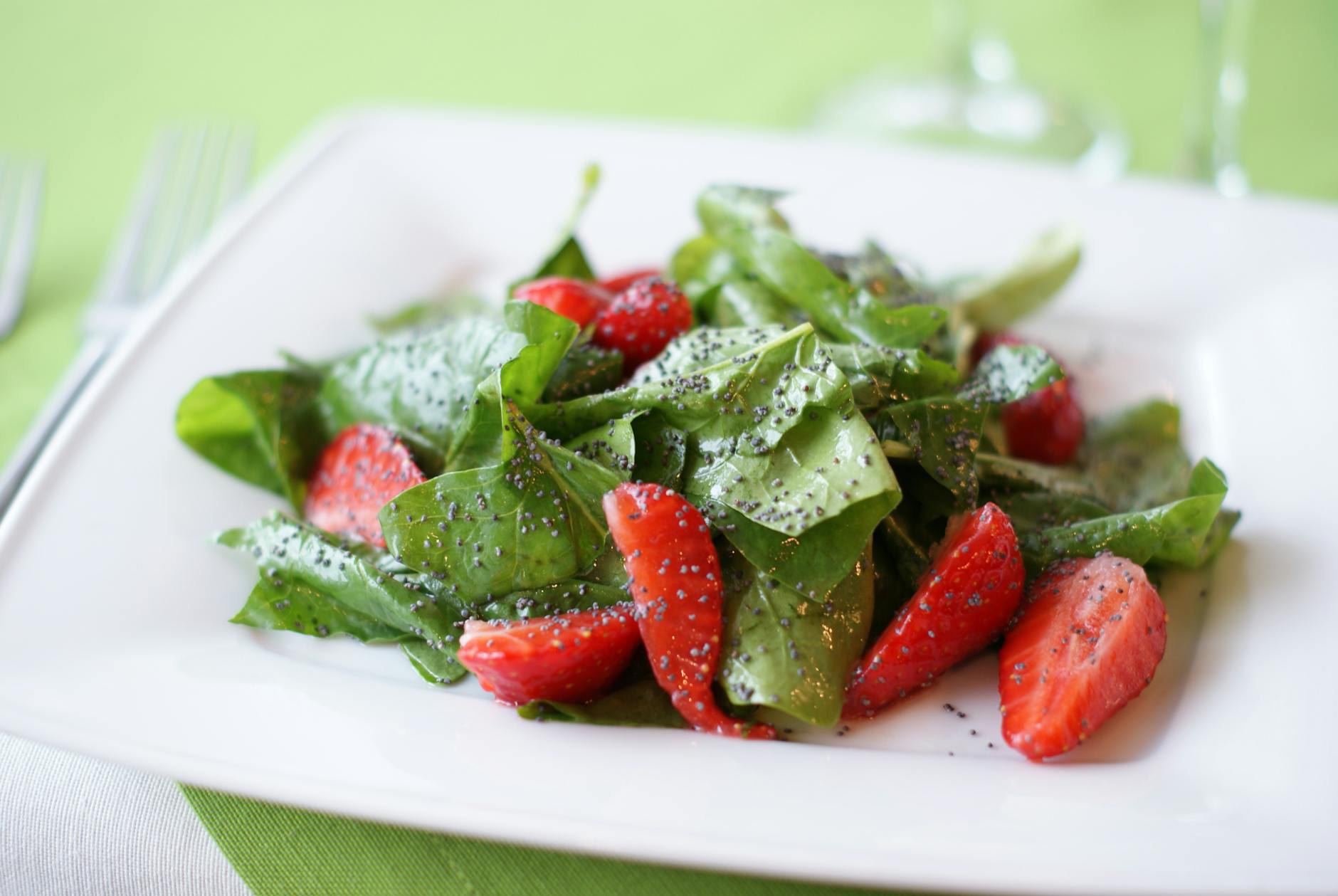 Colorful salad of fresh spinach and strawberries with poppy seeds on a plate. - vegan spring recipes