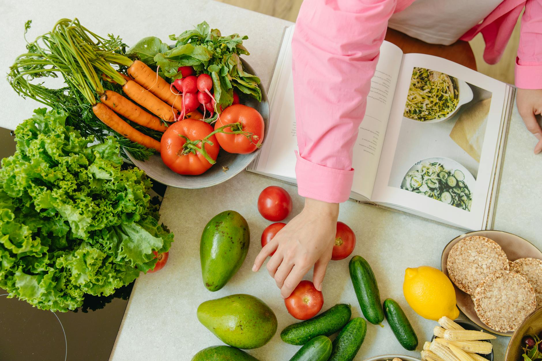 Top view of fresh vegetables and hands arranging them with a recipe book, promoting healthy eating. - vegan spring recipes