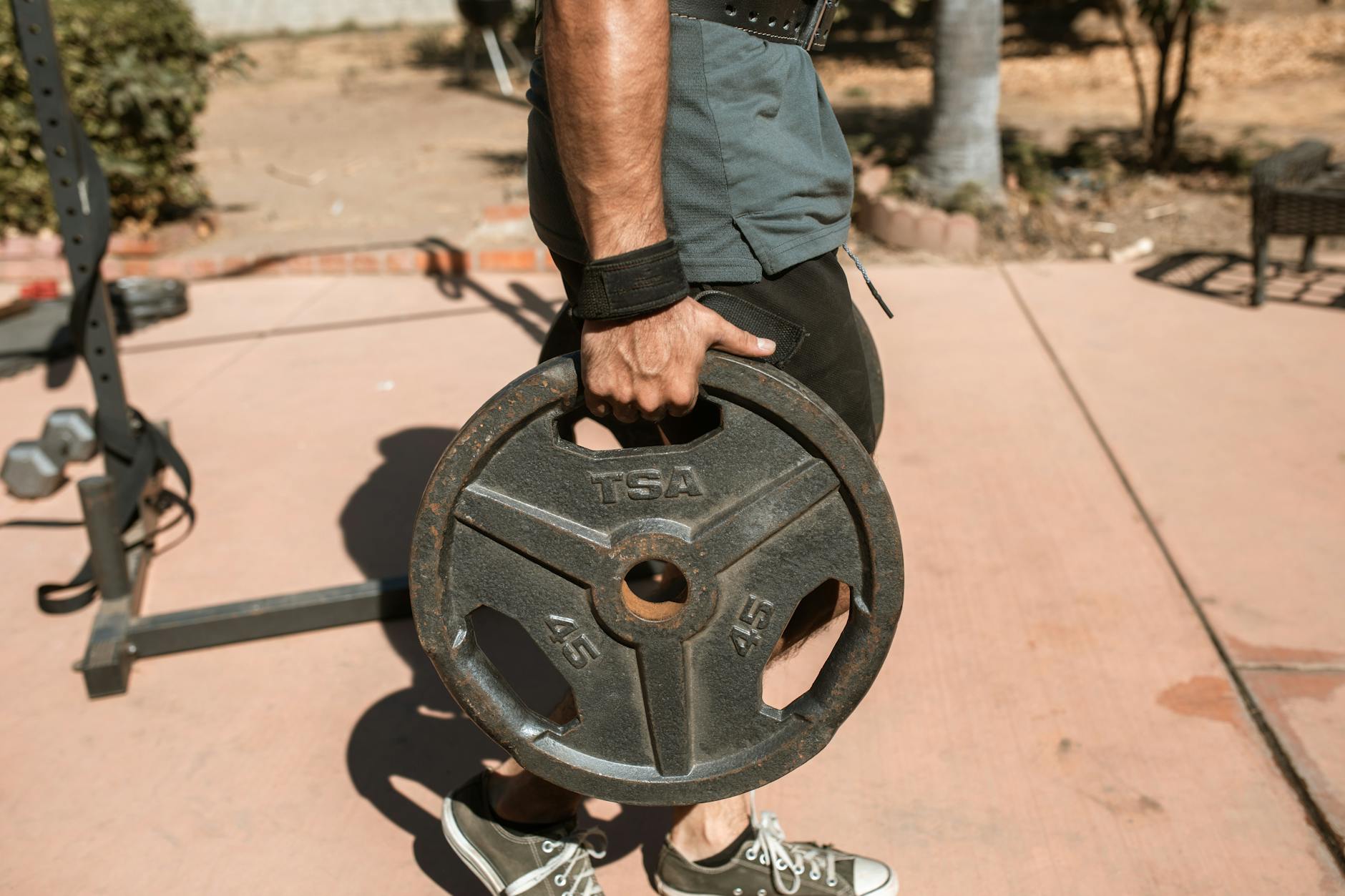 Close-up of a man's hand holding a 45lb weight plate outdoors during exercise. - weight training benefits
