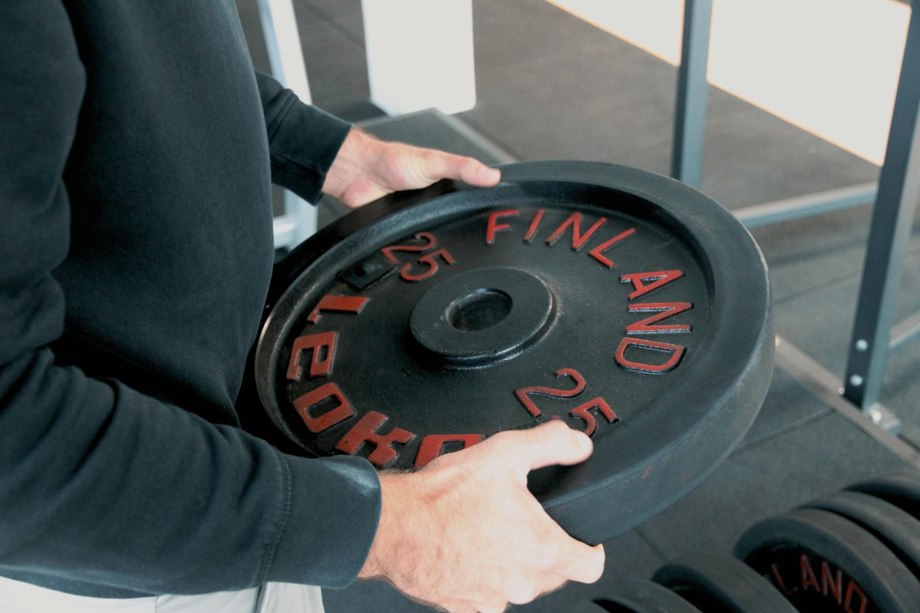 Close-up of a person holding a 25 kg weight plate in a gym. - weight training benefits
