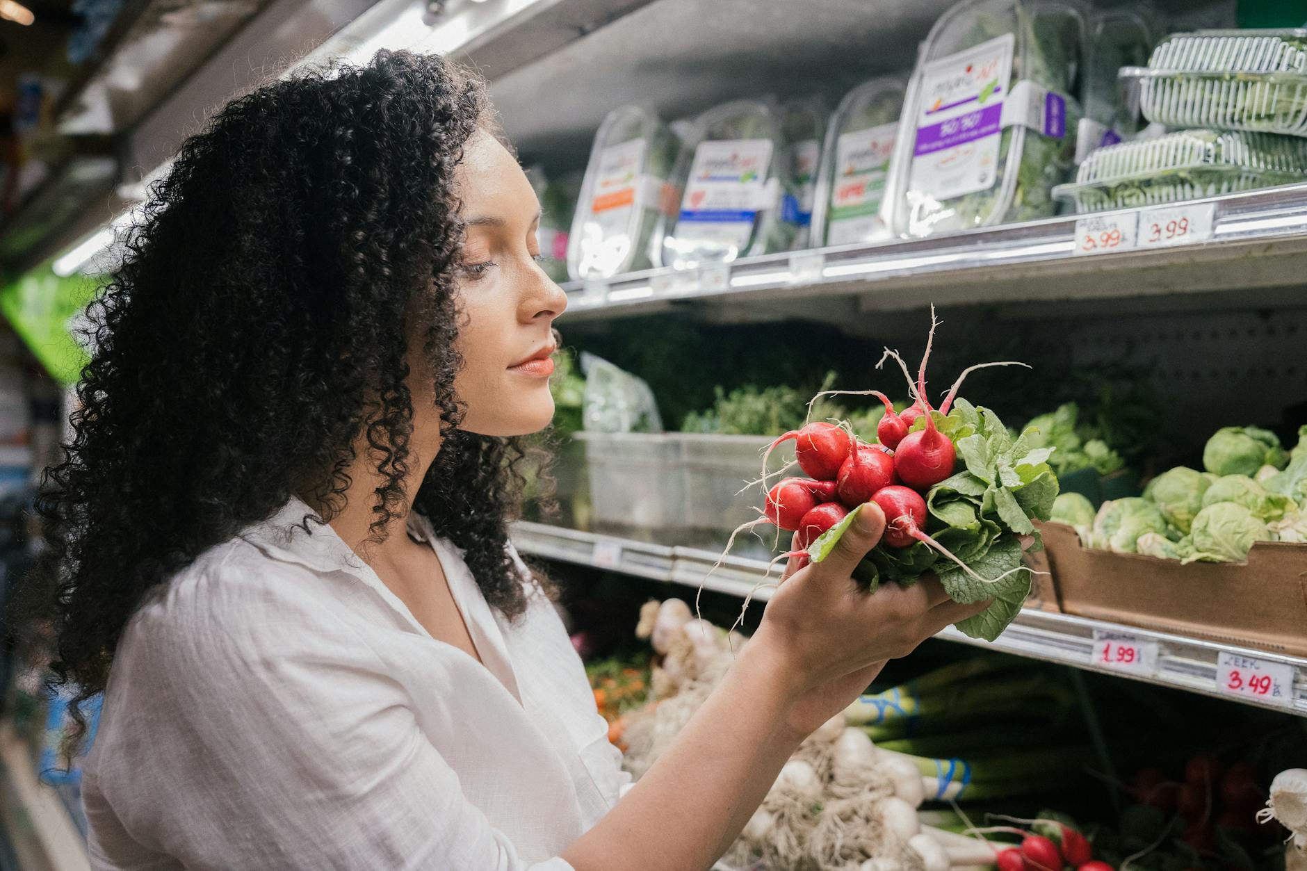 Woman in grocery store choosing fresh radishes from the vegetable aisle. - winter produce reset