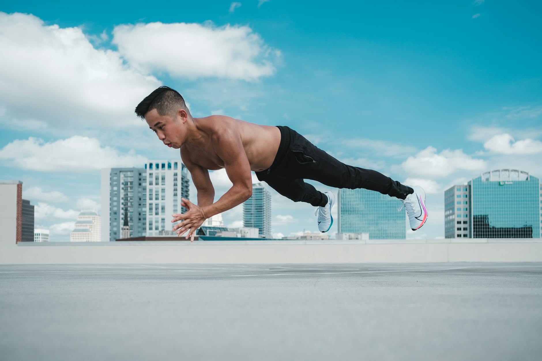 A muscular man performing a stretch on a rooftop with Orlando skyline in the background. - advanced core exercises