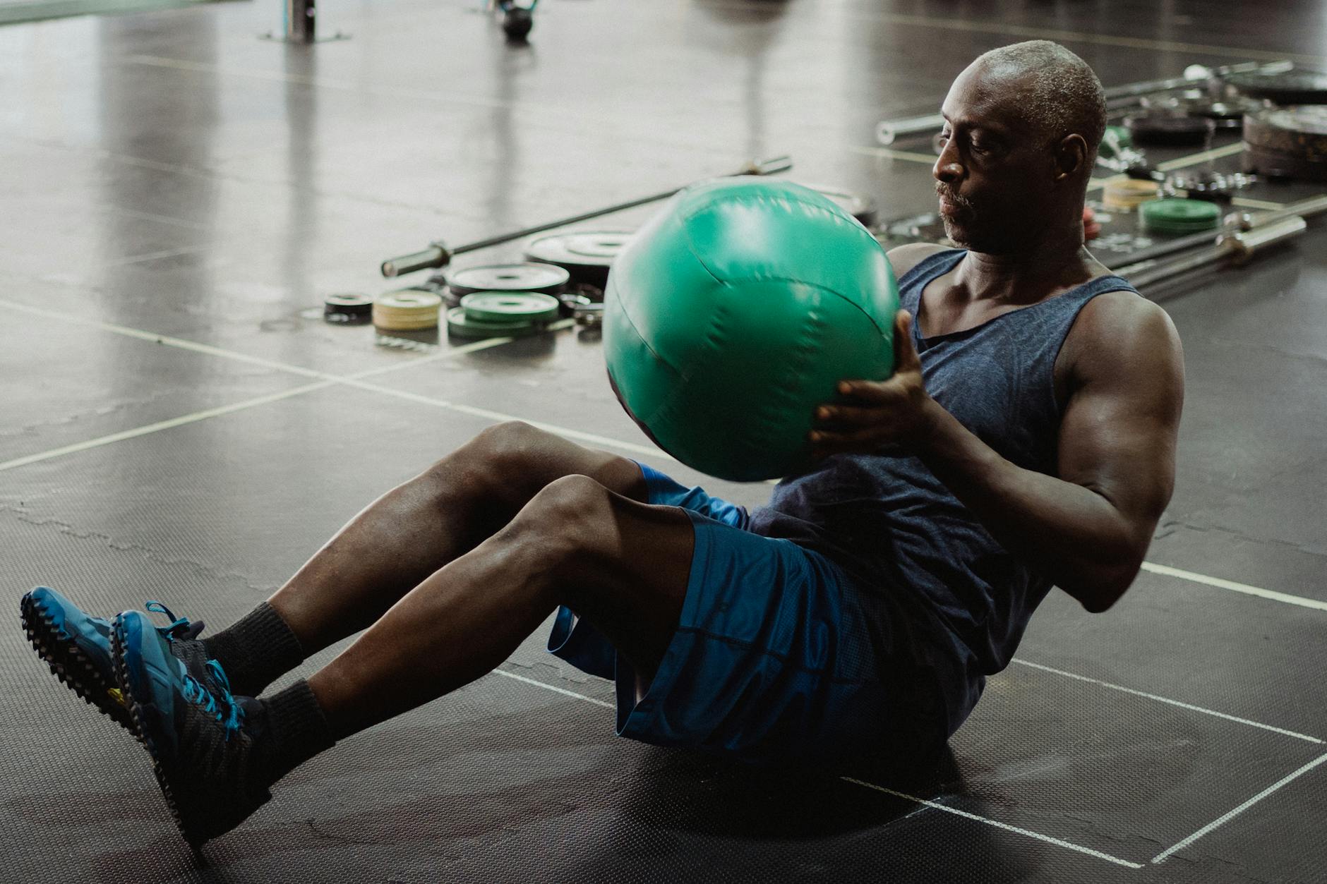 A focused African American man performs fitness exercises with a medicine ball at the gym - advanced core training