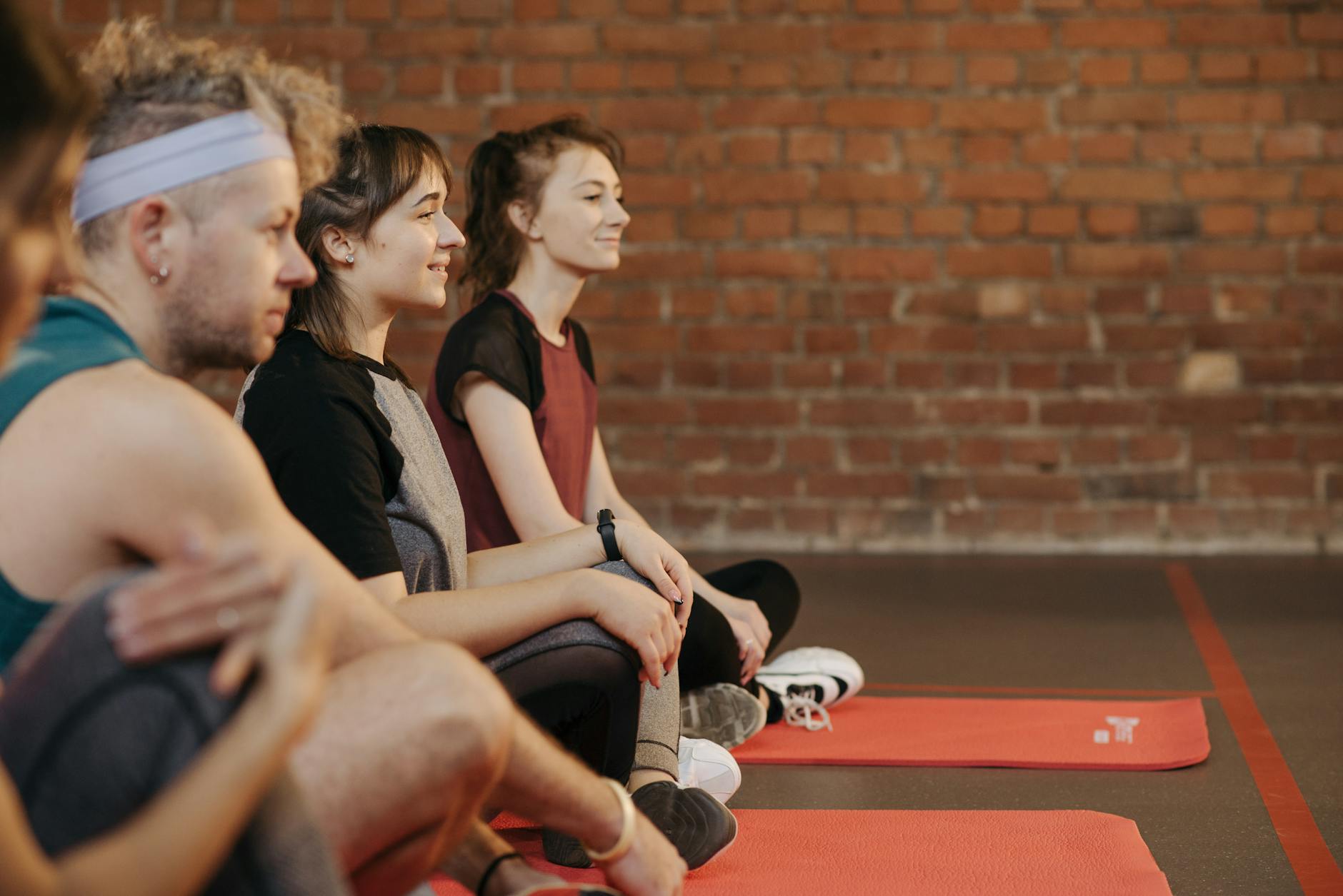 A diverse group of adults enjoying a yoga session on red mats in a studio with exposed brick walls. - balance exercise social life