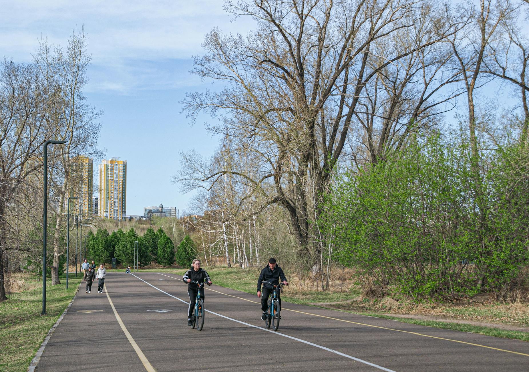People biking on a sunny day in a city park with skyscrapers in the background. - beginner bike rides spring