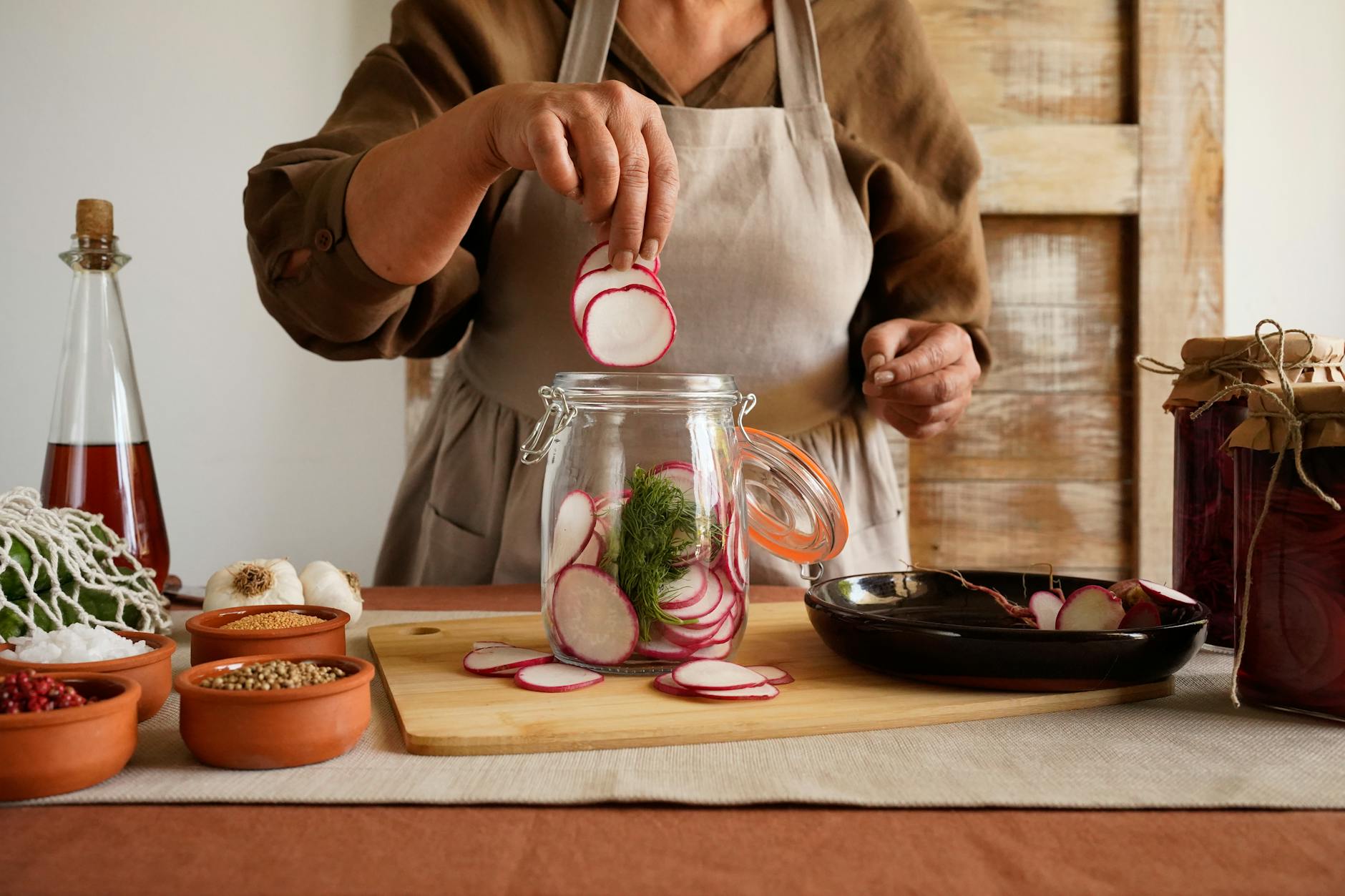 A woman preparing pickled radishes, showcasing ingredients in a rustic kitchen setting. - benefits of fermented foods
