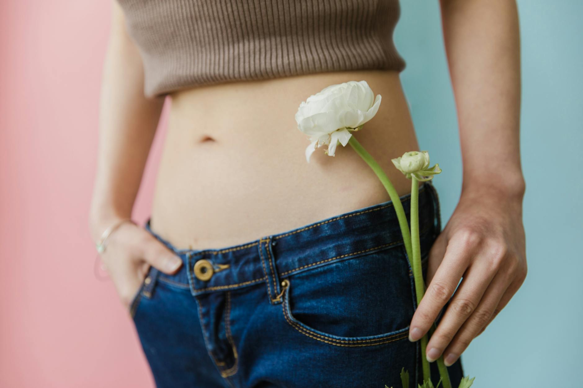 Close-up of a woman in a brown top and jeans holding a white flower. - bloating relief spring