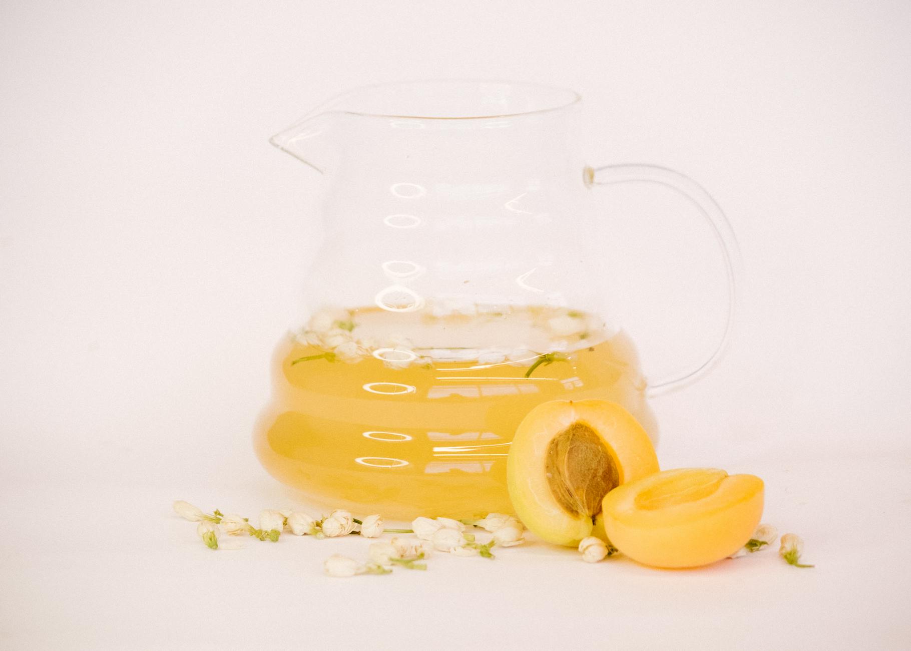 Glass pitcher of yellow jasmine peach infusion with fresh peaches and blossoms. - bloating relief spring