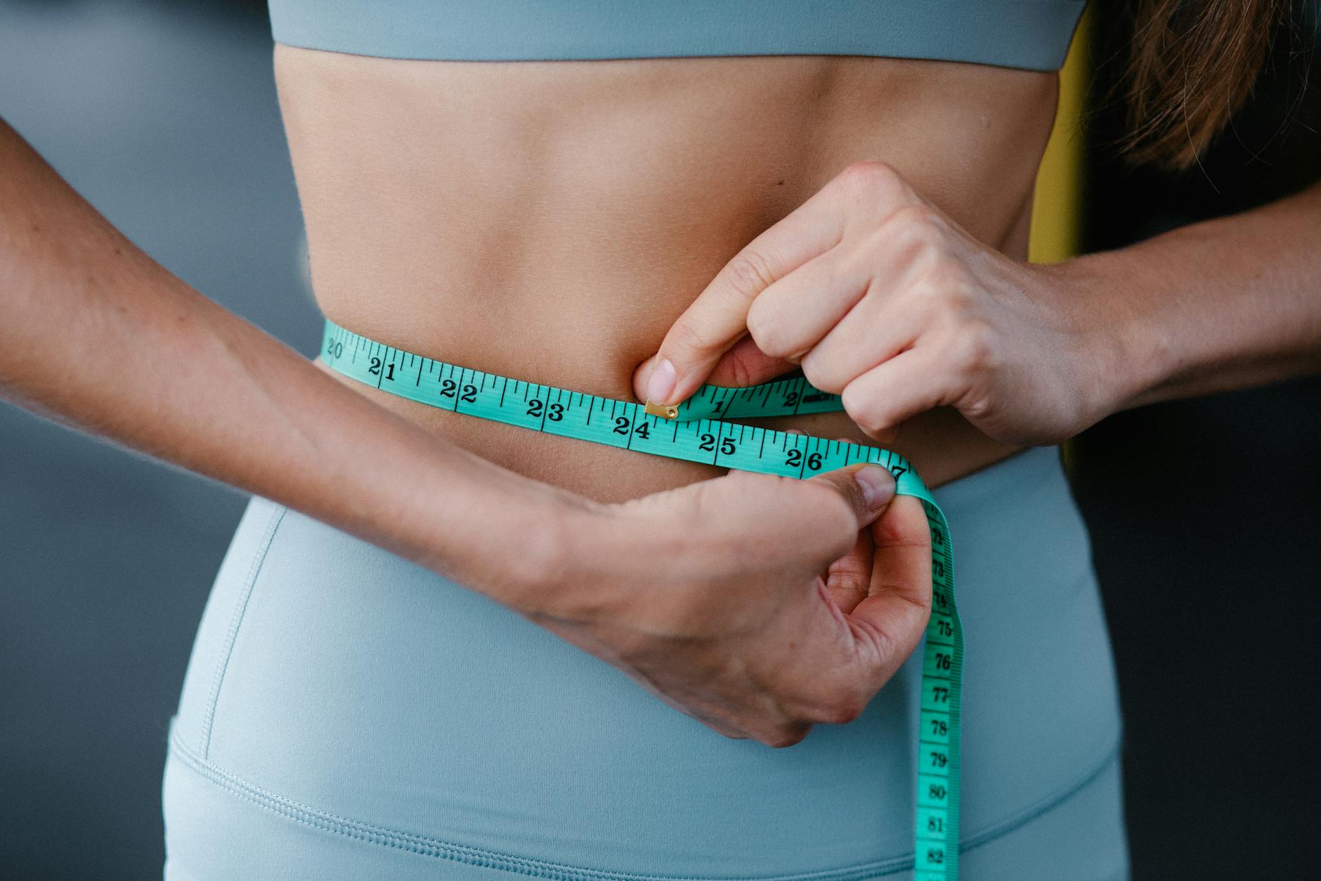 Close-up of a woman measuring her waist with a tape, representing fitness, health, and weight loss. - boost metabolism fat loss