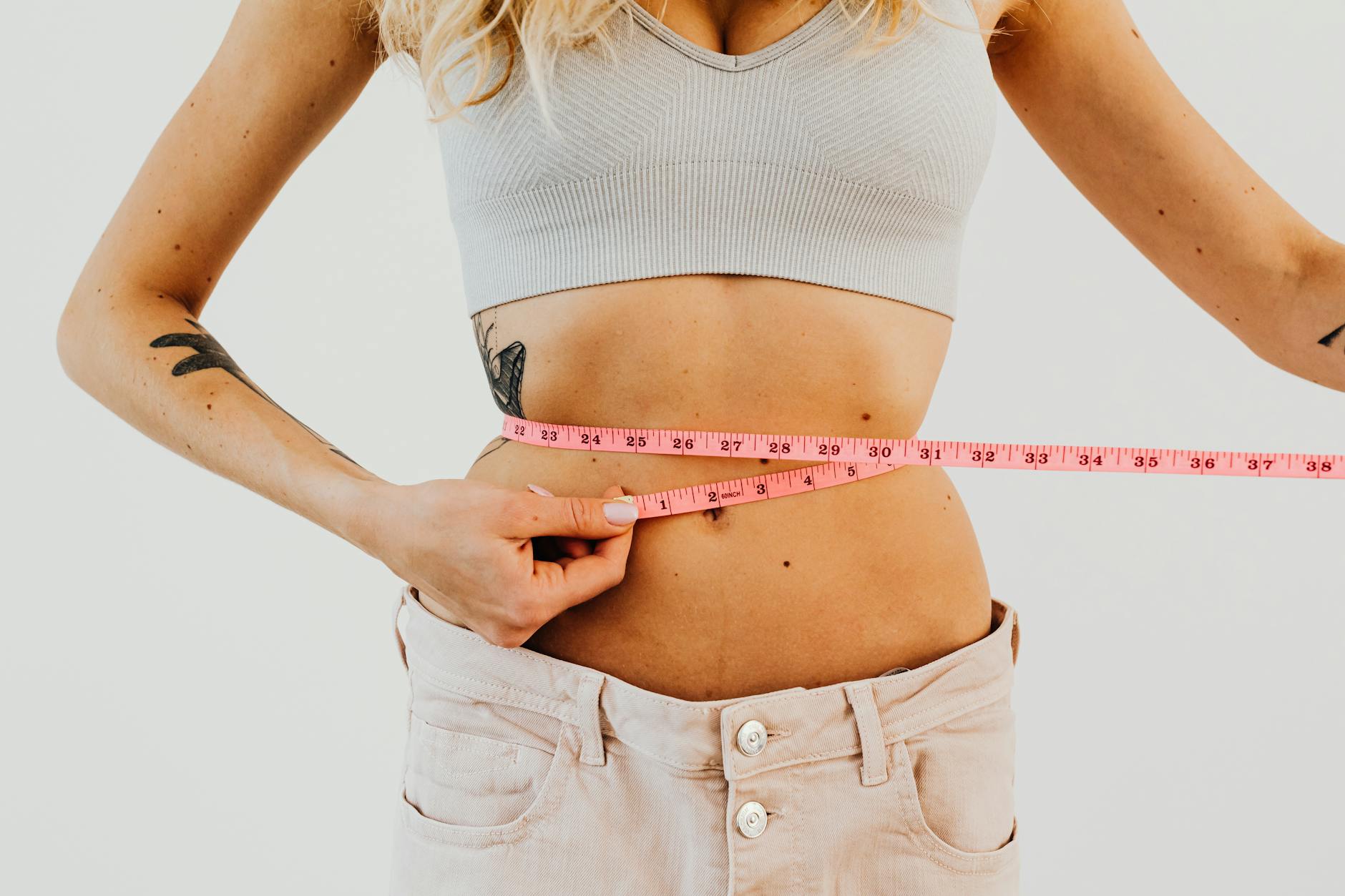 Close-up of woman in sports bra measuring waist with pink tape for fitness goals. - boost metabolism fat loss