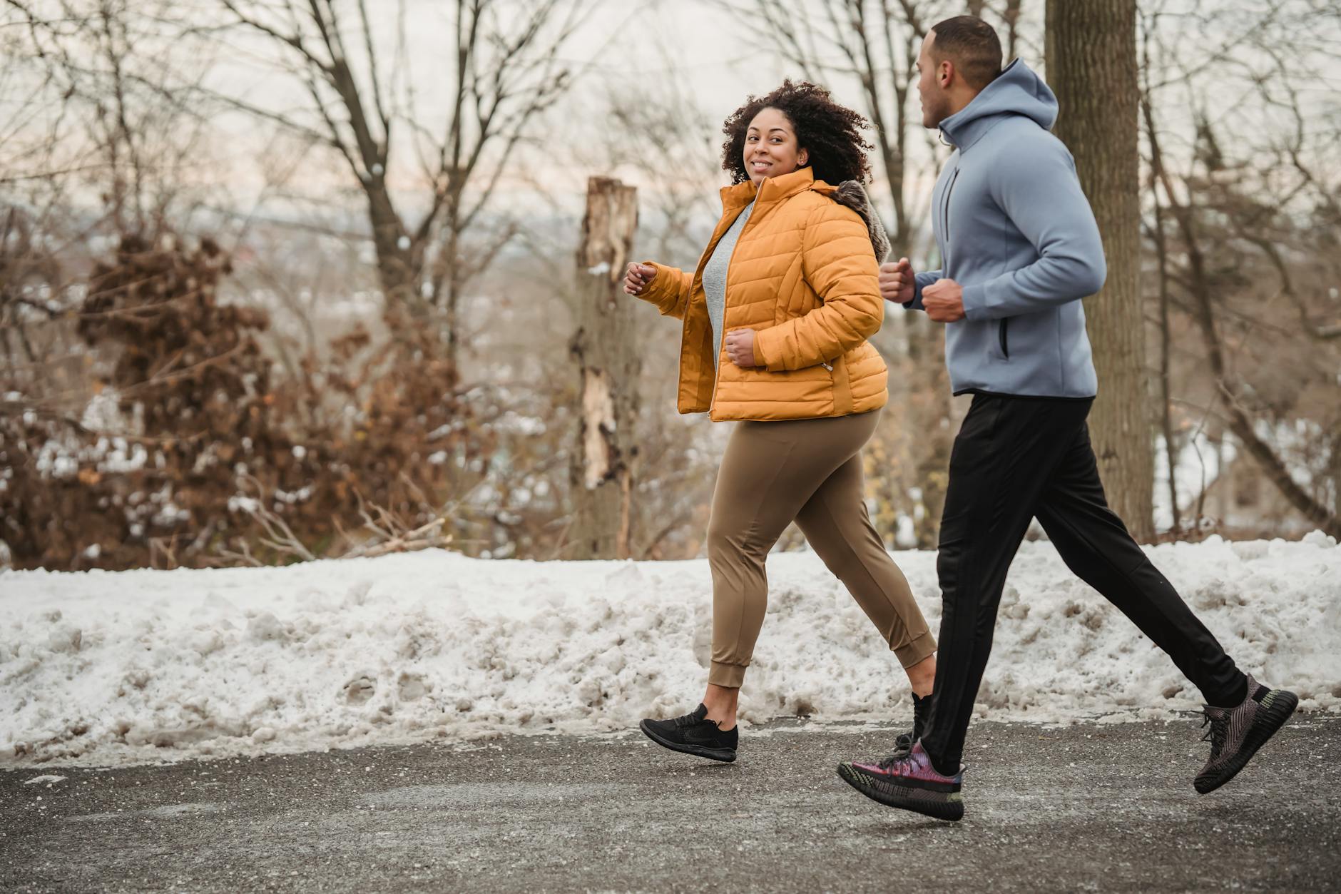 Full body of positive curvy African American woman and black coach looking at each other while jogging on asphalt walkway in winter time - cardio for weight loss