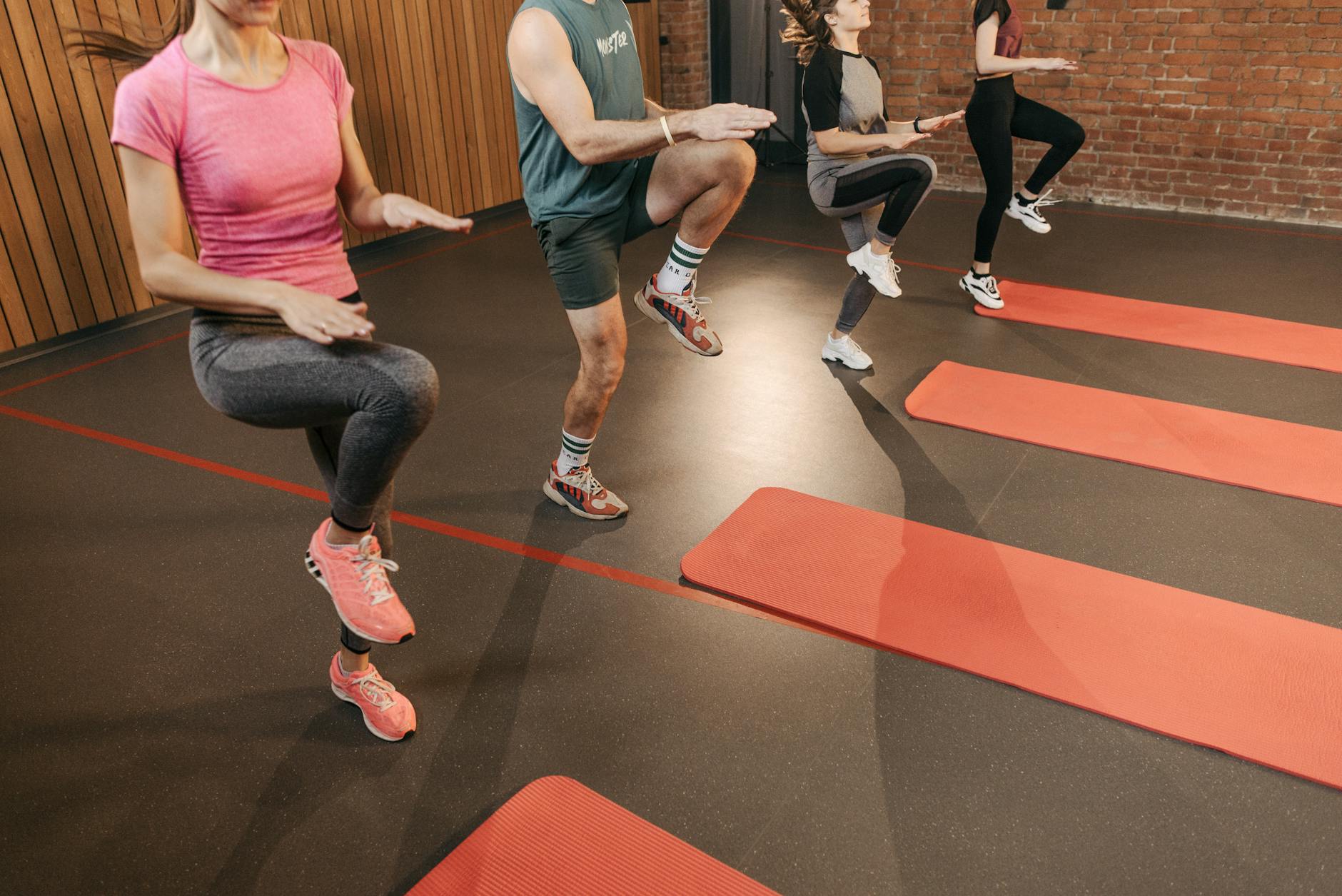 A group performs high knees together in an indoor fitness studio with yoga mats. - may cardio workouts