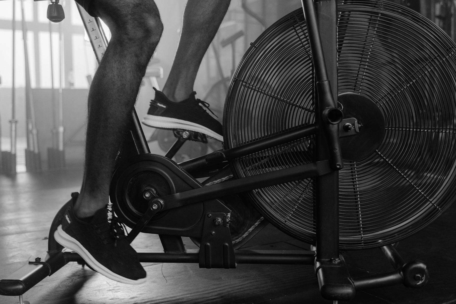 Black and white image of person using exercise bike in a gym setting. - may cardio workouts
