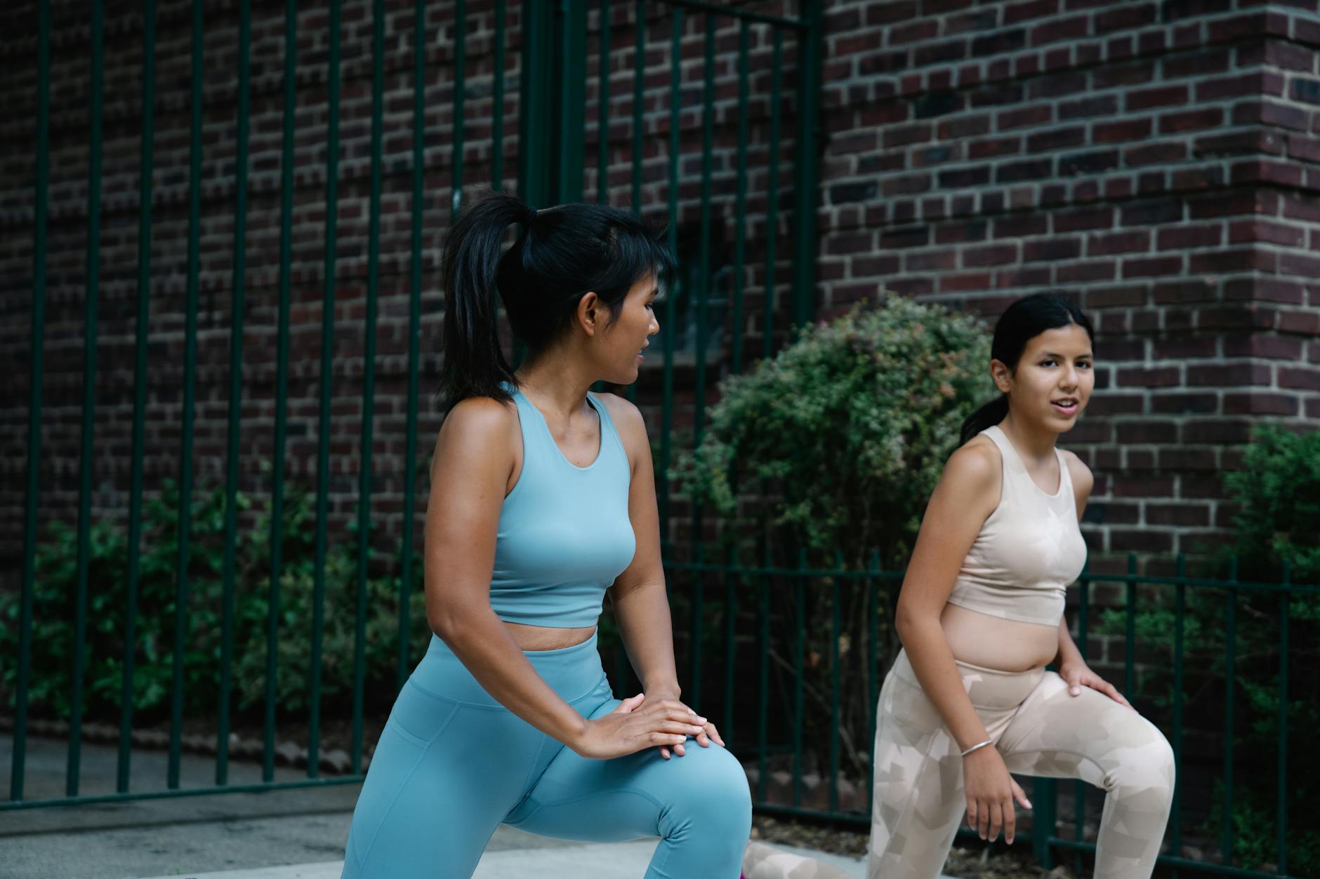 Mother and daughter stretching on the sidewalk in sports clothing, focused on fitness. - daily workout plan