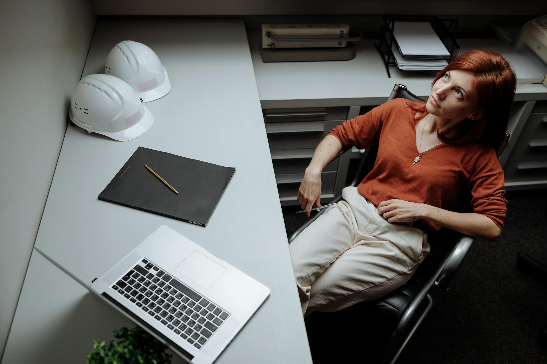 Professional woman relaxing at desk with laptop, hard hats, and documents, contemplating ideas. - desk exercises