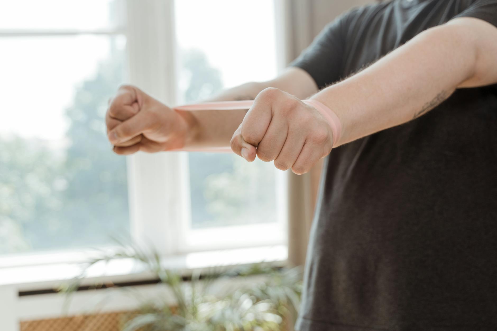 A man uses a resistance band for arm exercises in a bright indoor setting. - desk exercises