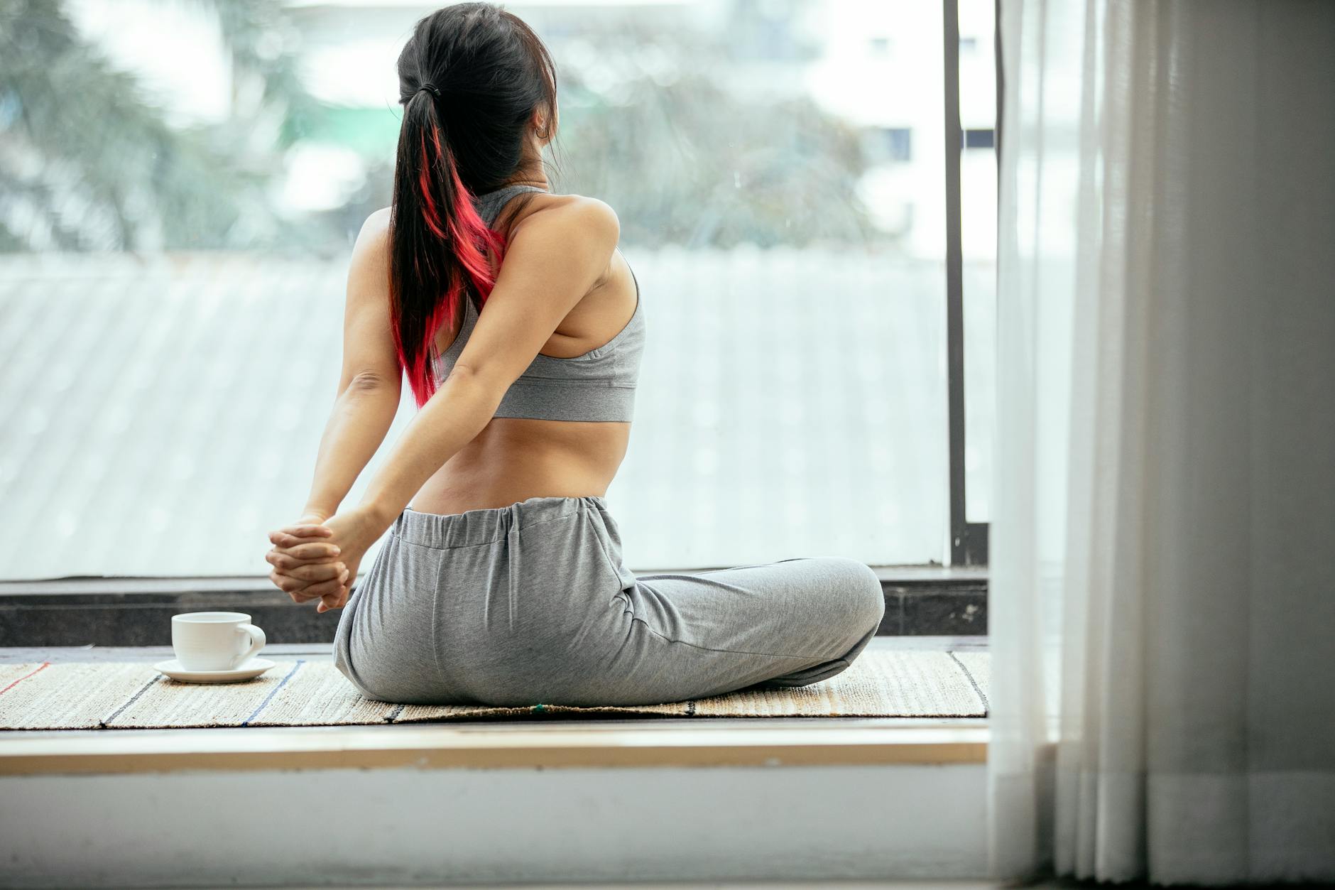 Back view of slim unrecognizable female sitting on mat and stretching arms behind back while doing warm up exercise in morning on terrace - desk stretches