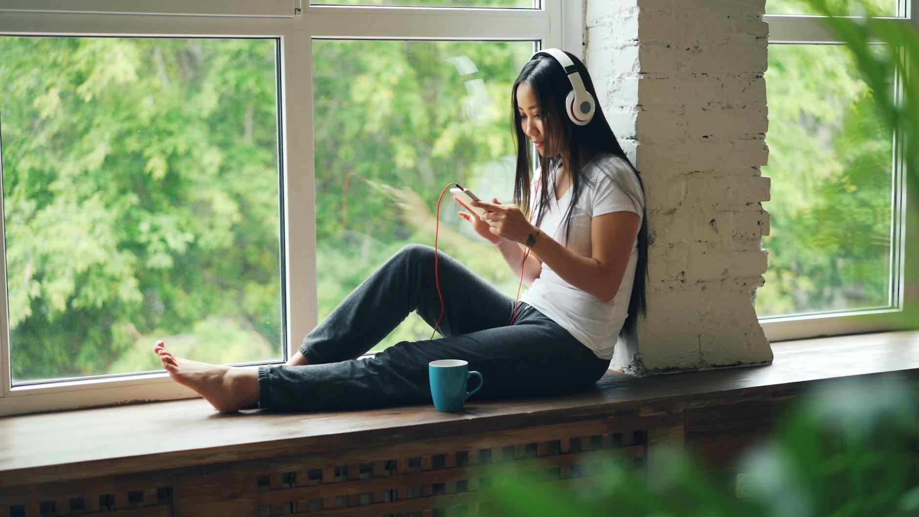 Woman listening to music on headphones, enjoying a peaceful moment by the window. - digital declutter spring