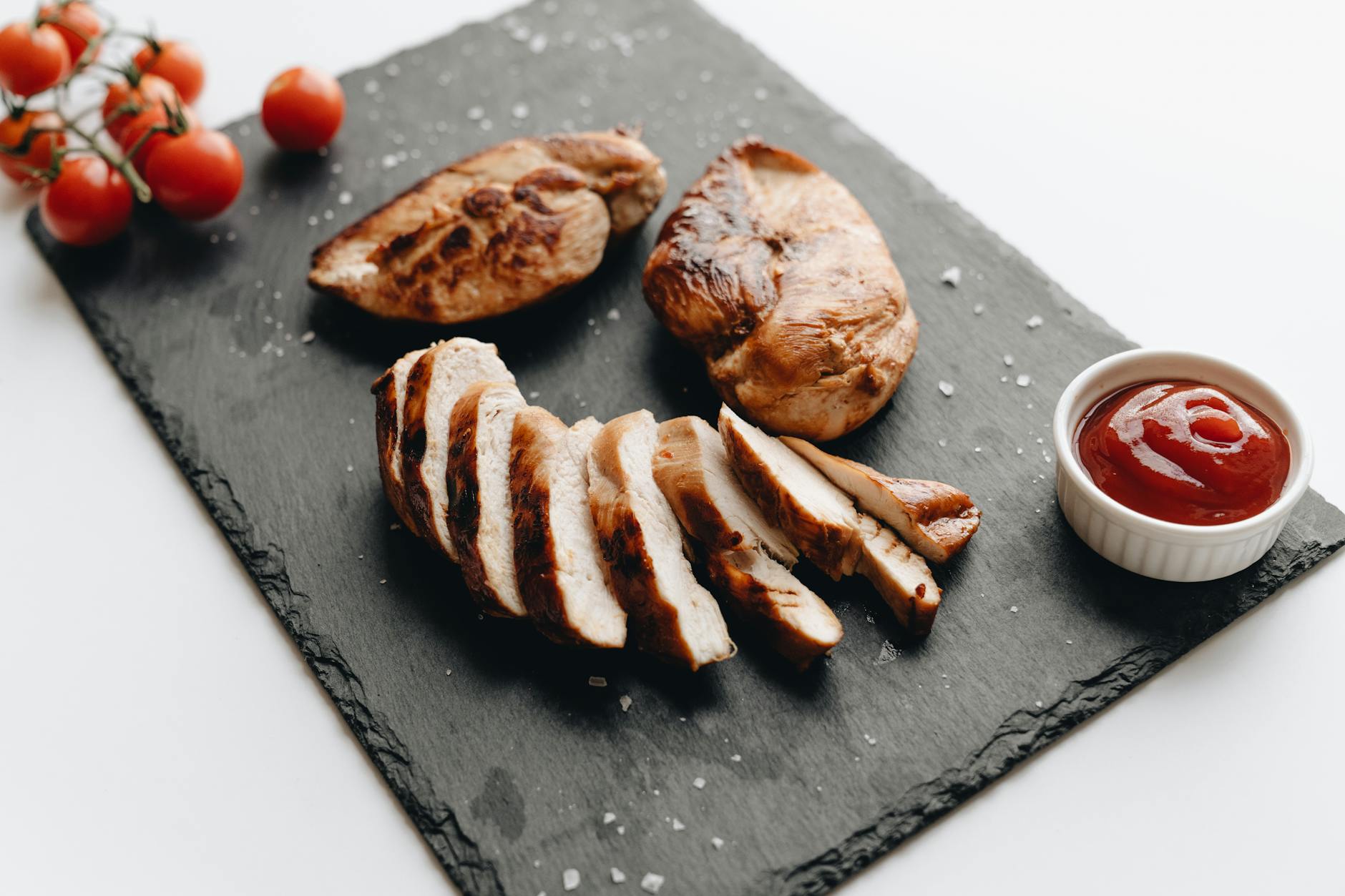 Sliced grilled chicken breast on slate with cherry tomatoes and dipping sauce. - easy chicken recipes