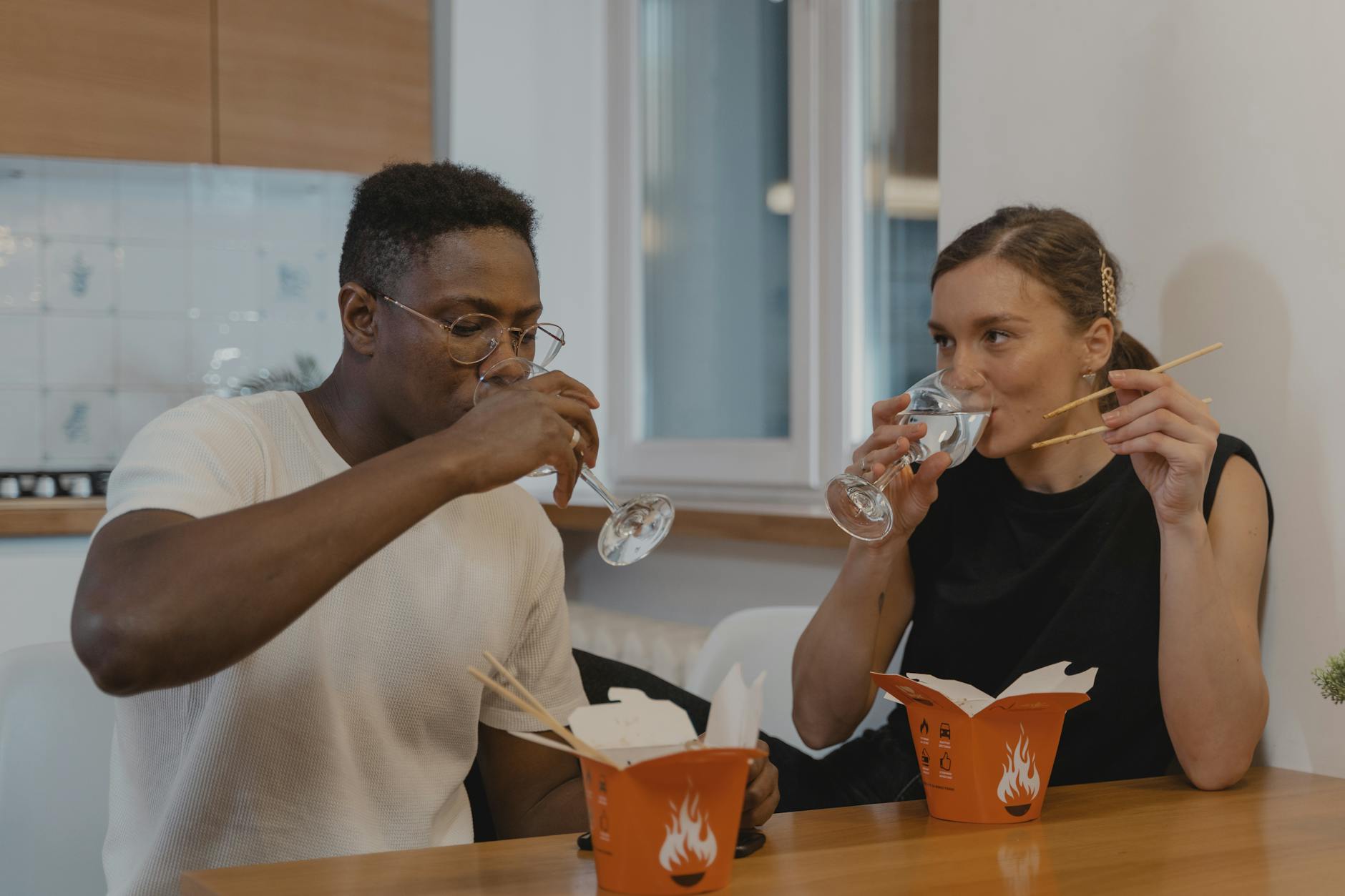 An interracial couple drinking water and eating takeout food at home. - easy dinner for two