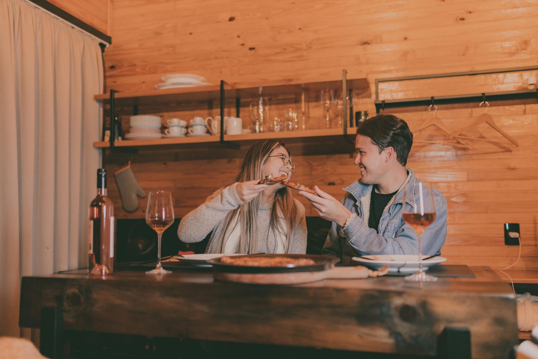 A couple enjoying pizza and wine at a rustic wooden table in a cozy setting. - easy dinner for two