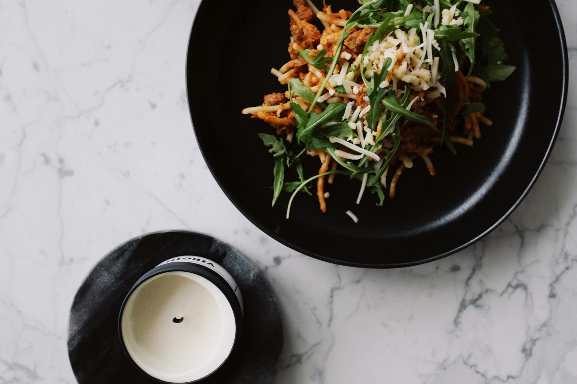 Tasty spaghetti with arugula and cheese served on a black plate on a marble table. - easy weeknight dinners