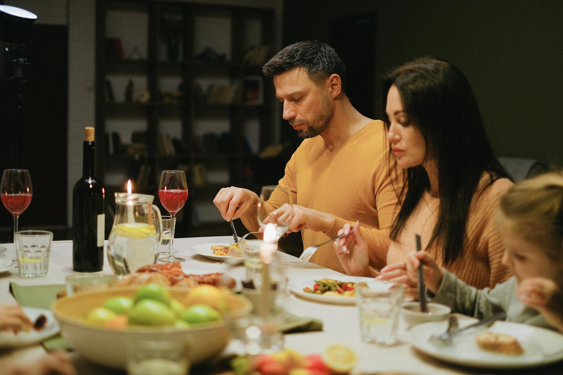 A family gathered around a dinner table indoors, enjoying a meal together with wine and candles. - easy weeknight dinners