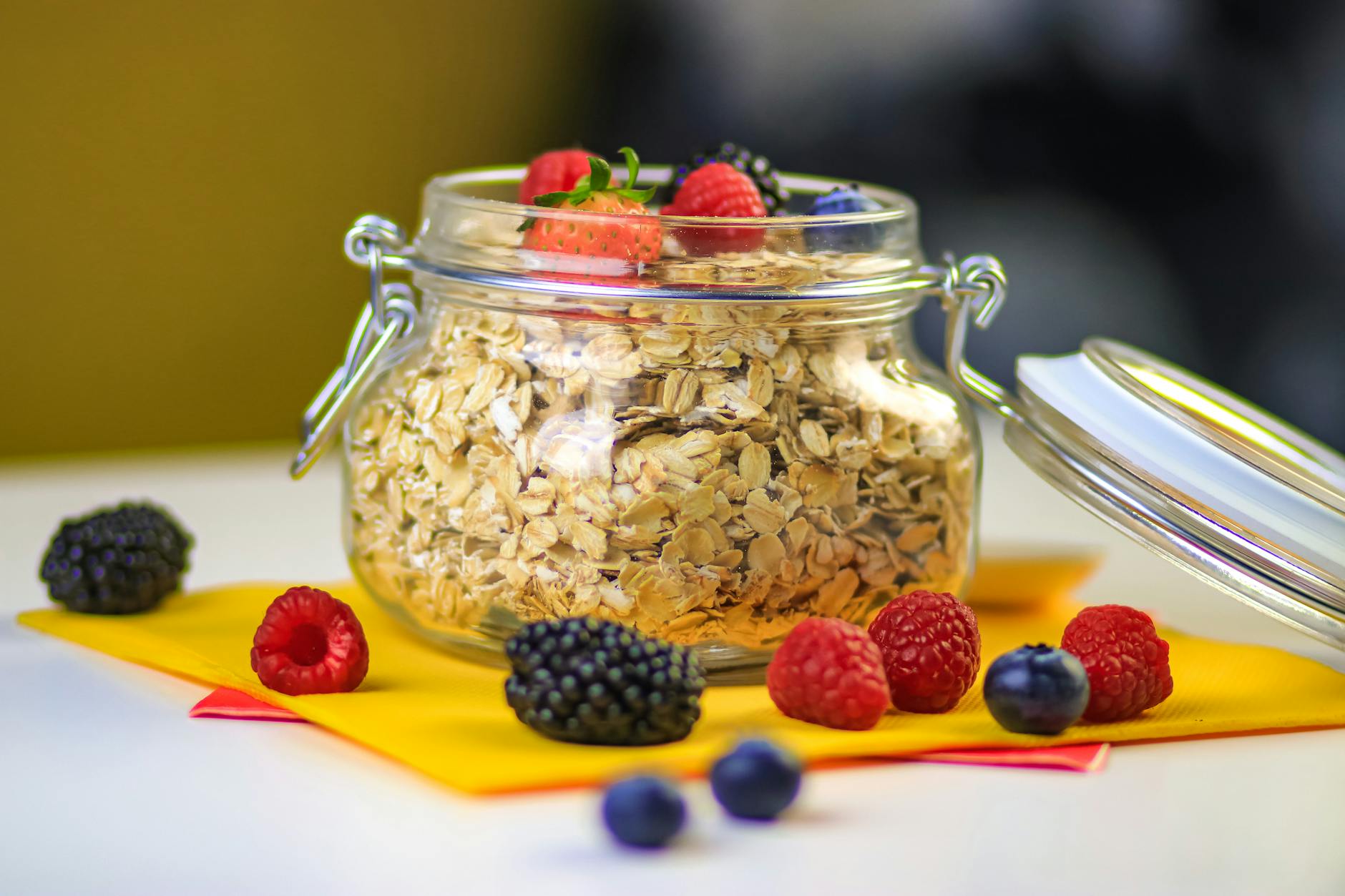 Glass jar of oats surrounded by fresh berries on a colorful background. - energy boosting foods