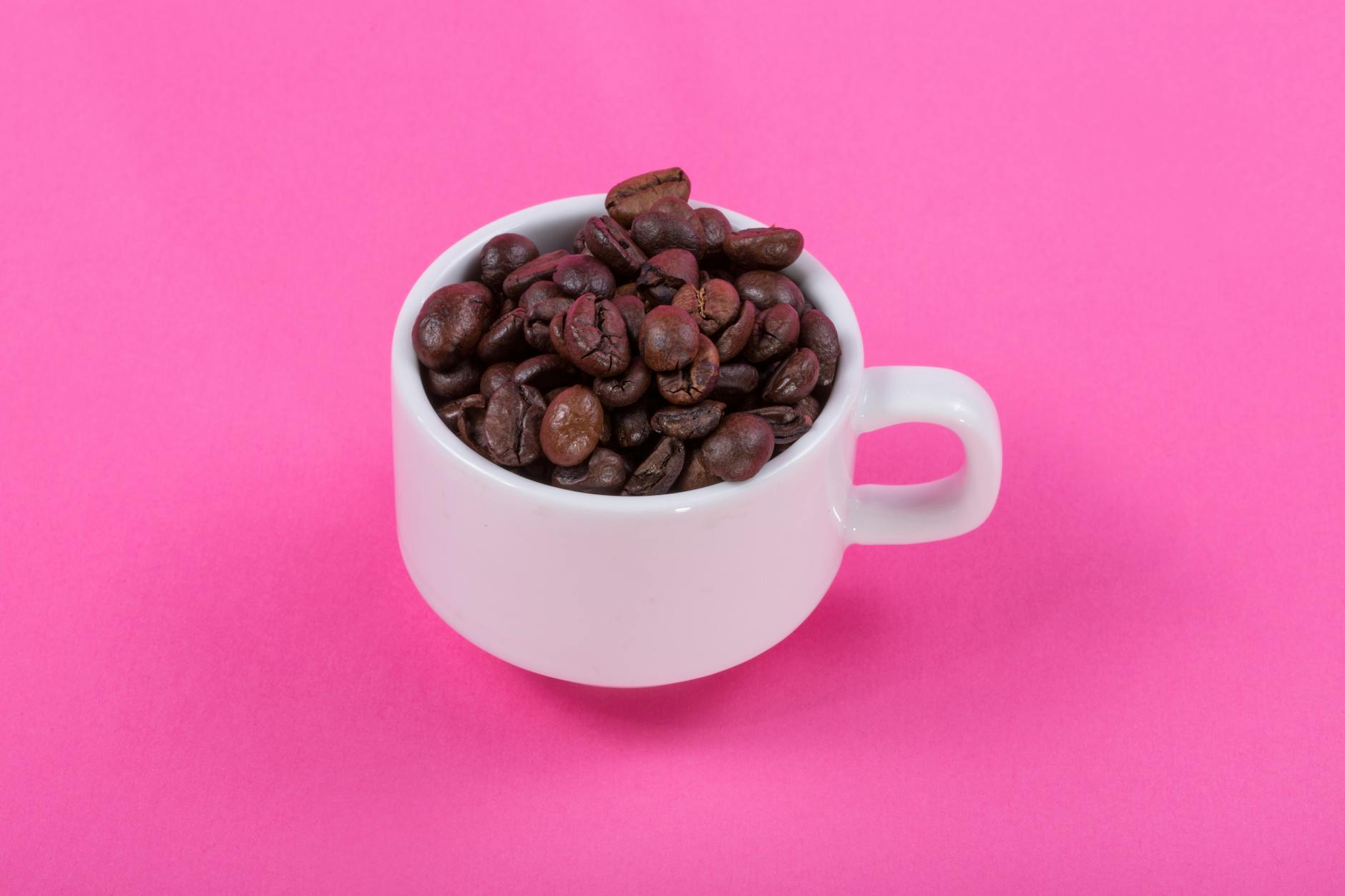 A cup filled with roasted coffee beans on a vibrant pink backdrop, perfect for a coffee-themed design. - energy boosting foods