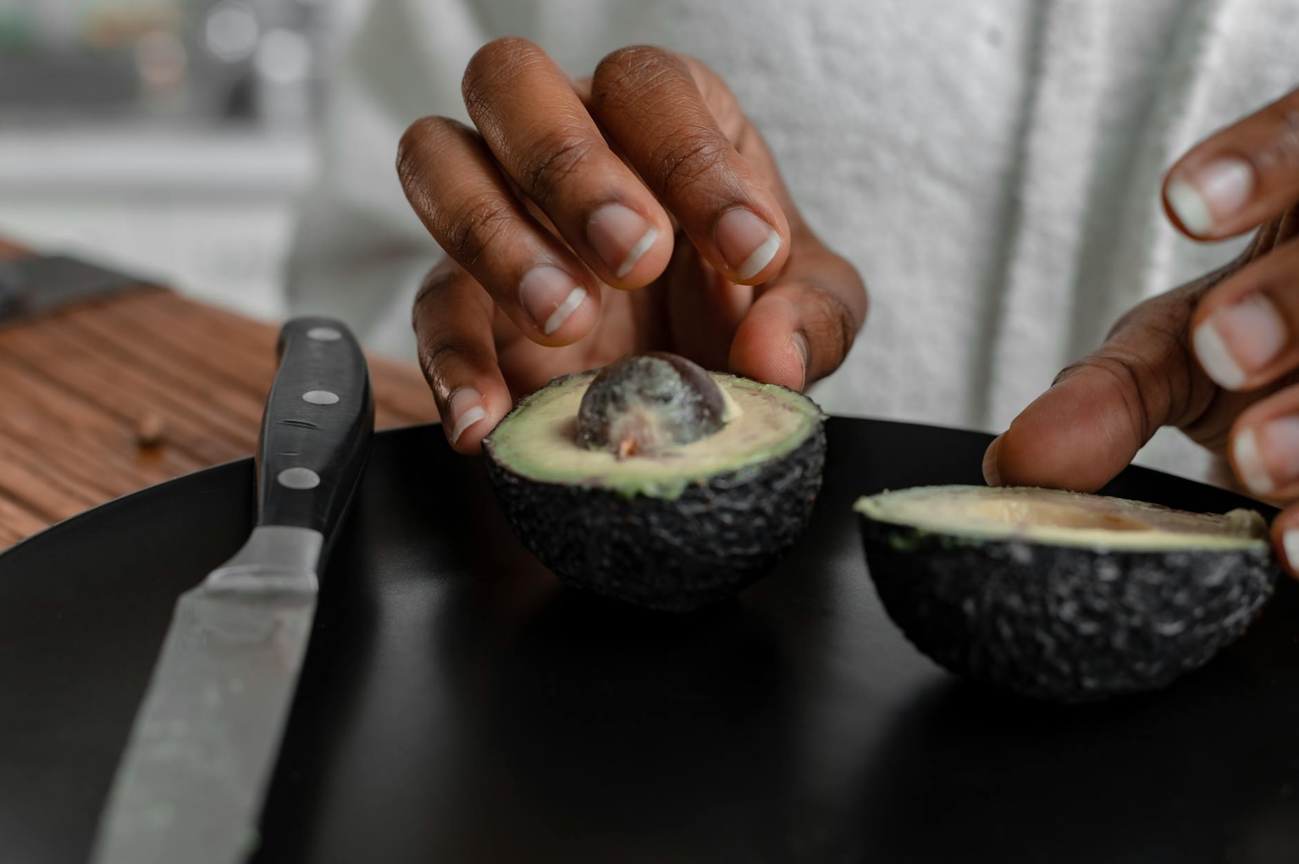 Hands slicing a fresh avocado on a black plate. Ideal for food blogs. - glowing skin foods