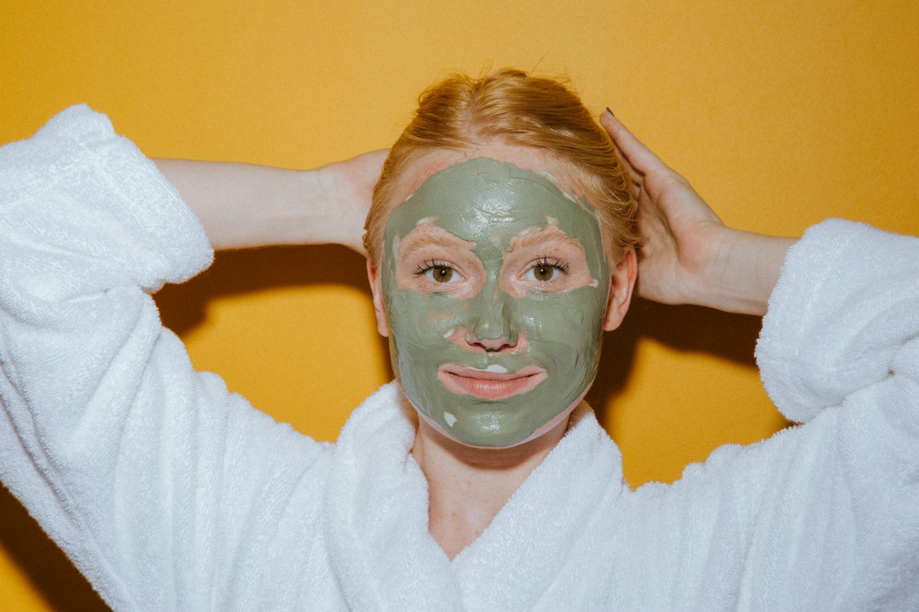 Woman enjoying self-care with a green face mask against a yellow background. - glowing skin recipes