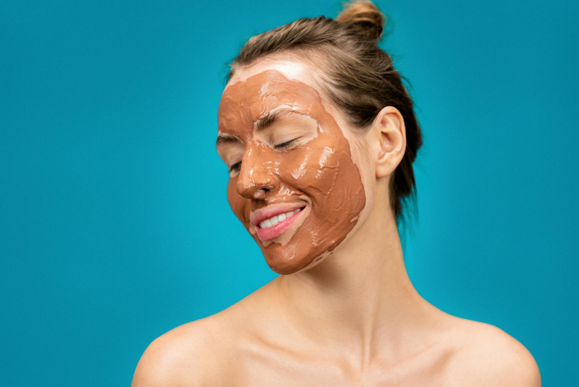 A woman smiles while applying a clay mud mask for skincare treatment. - glowing skin recipes