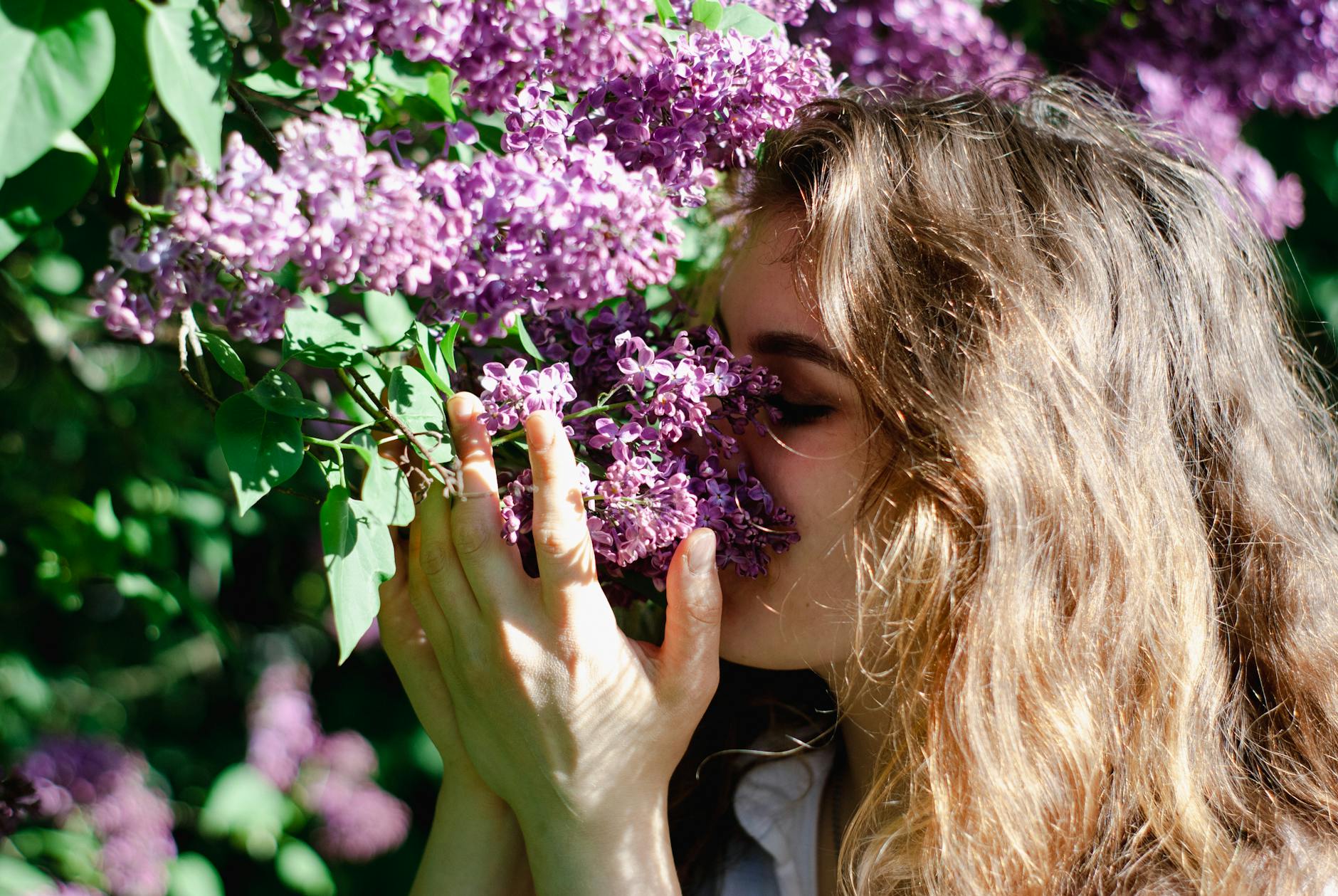 A young woman relishes the scent of lilac flowers in a sunlit garden, embodying spring and relaxation. - gut health allergies